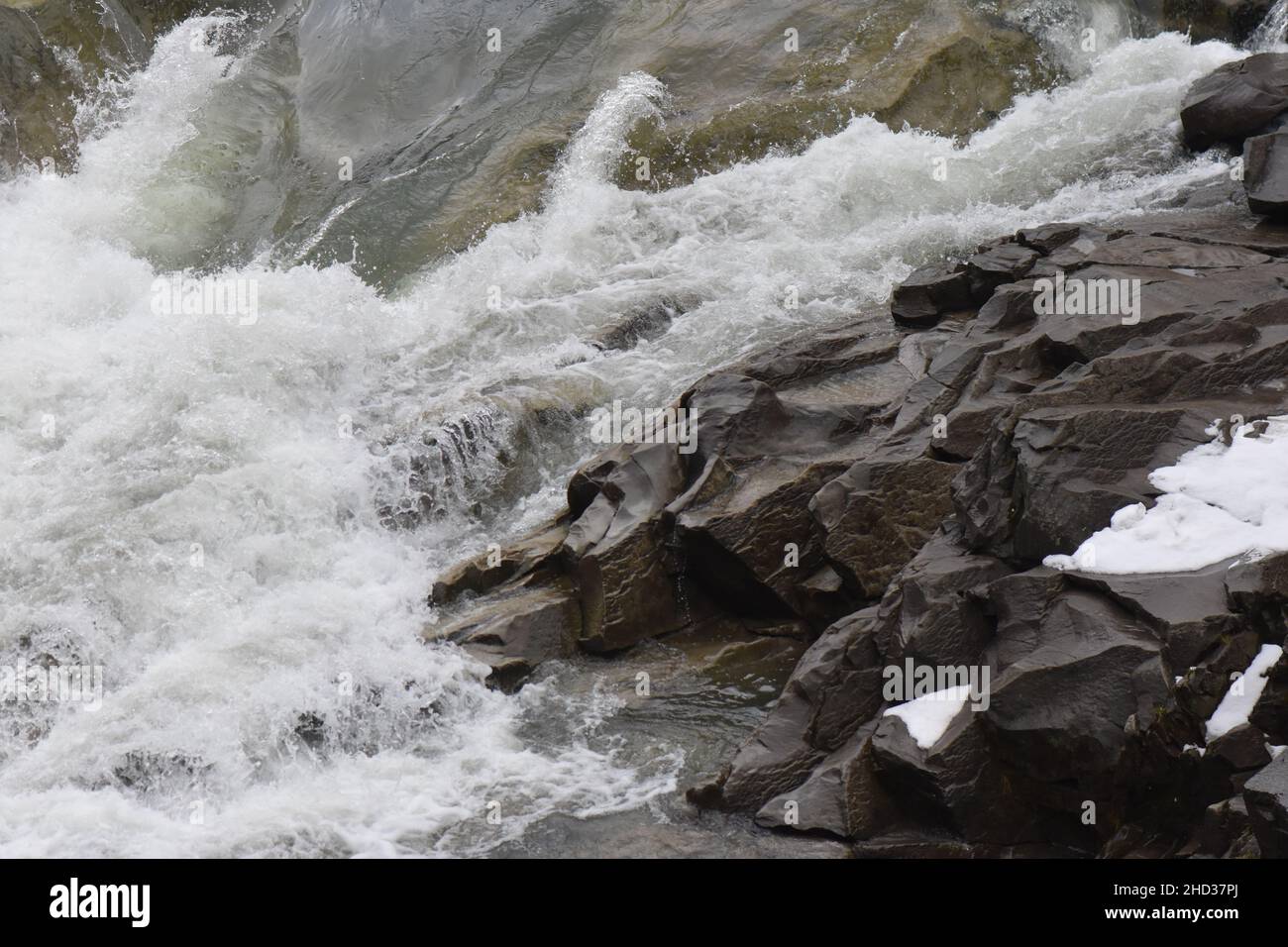 Primo piano di un fiume schiumoso e che scorre lungo le rocce in inverno Foto Stock