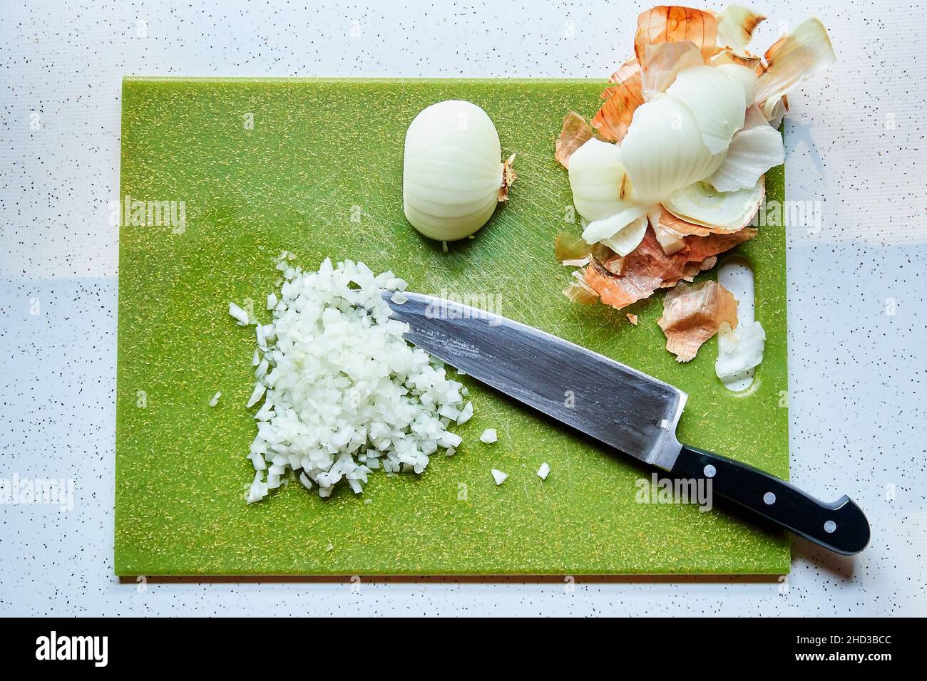 Vista dall'alto della cipolla tagliata a dadini e del coltello dello chef sul tagliere di plastica verde Foto Stock
