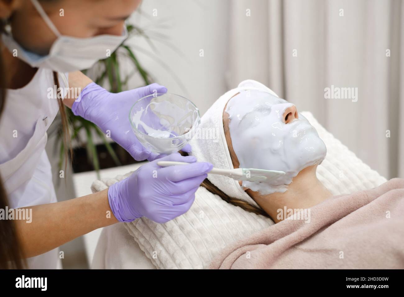 Il cosmetologo applica la maschera della pelle con pennello, cura e procedura di trattamento in clinica estetica moderna. Donna tratta la pelle in salone di bellezza, anti-età non Foto Stock