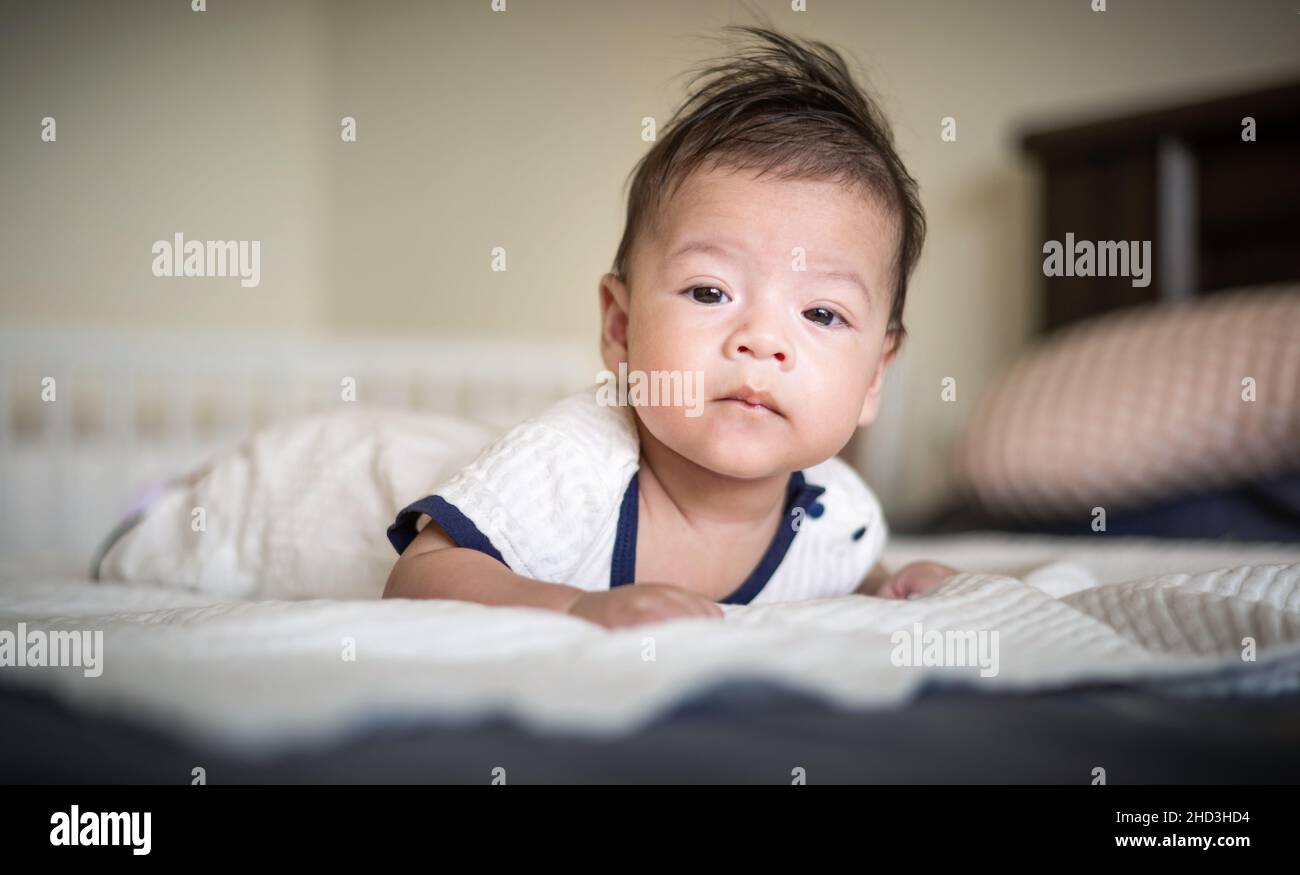 Adorabile 2 mesi di razza mista neonato ragazzo sdraiato sul pancino sul letto sollevare testa e giocare Foto Stock