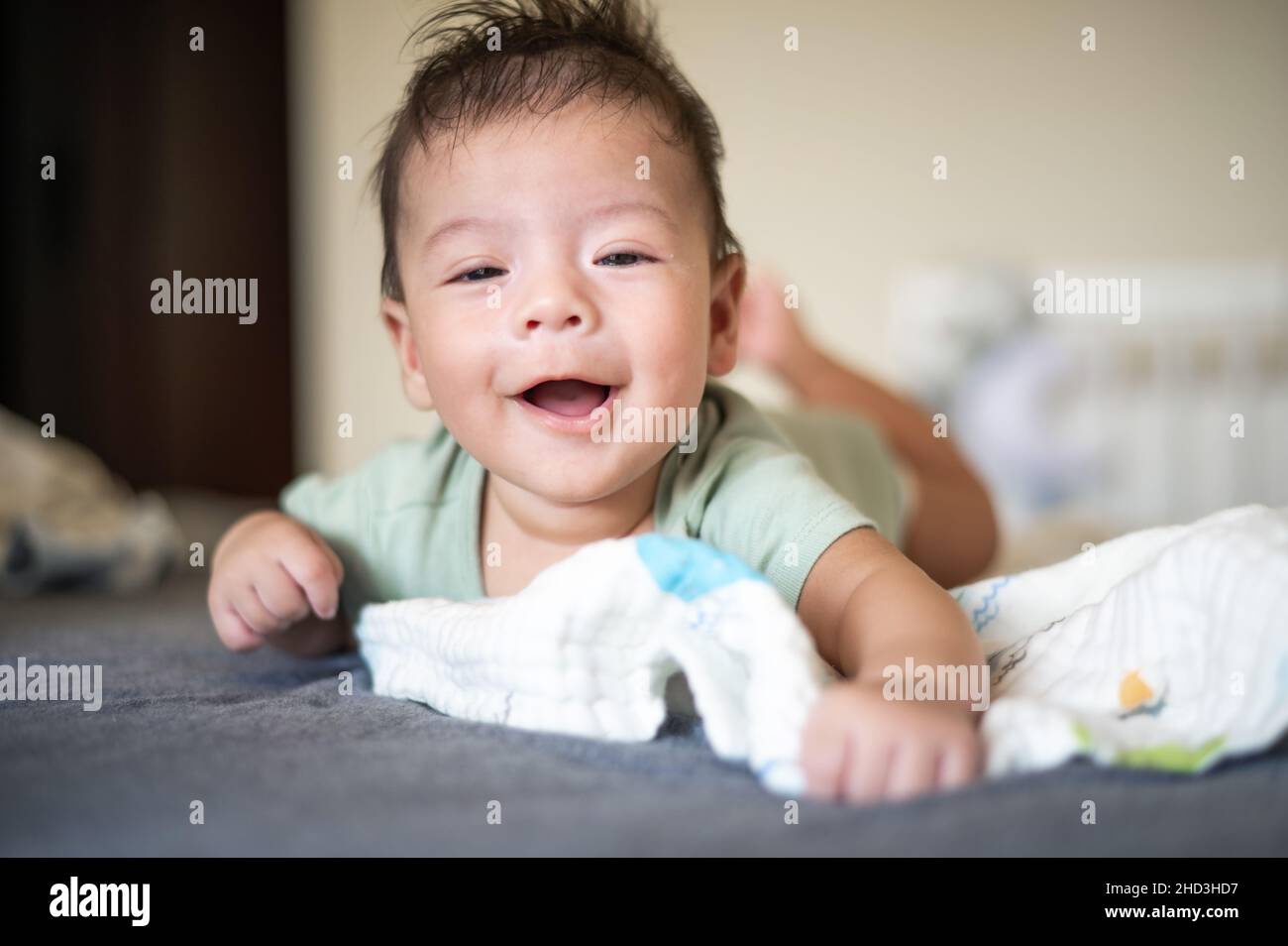 Adorabile 2 mesi di razza mista neonato ragazzo sdraiato sul pancino sul letto sollevare testa e sorridente Foto Stock