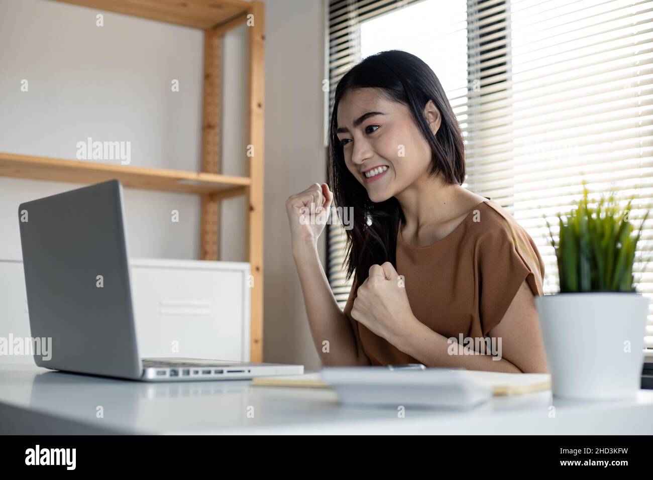 Giovane donna asiatica che gioca online sui social network con un computer portatile felice in camera di lavoro a casa. Donna felice che gioca a internet online su un notebook. Foto Stock