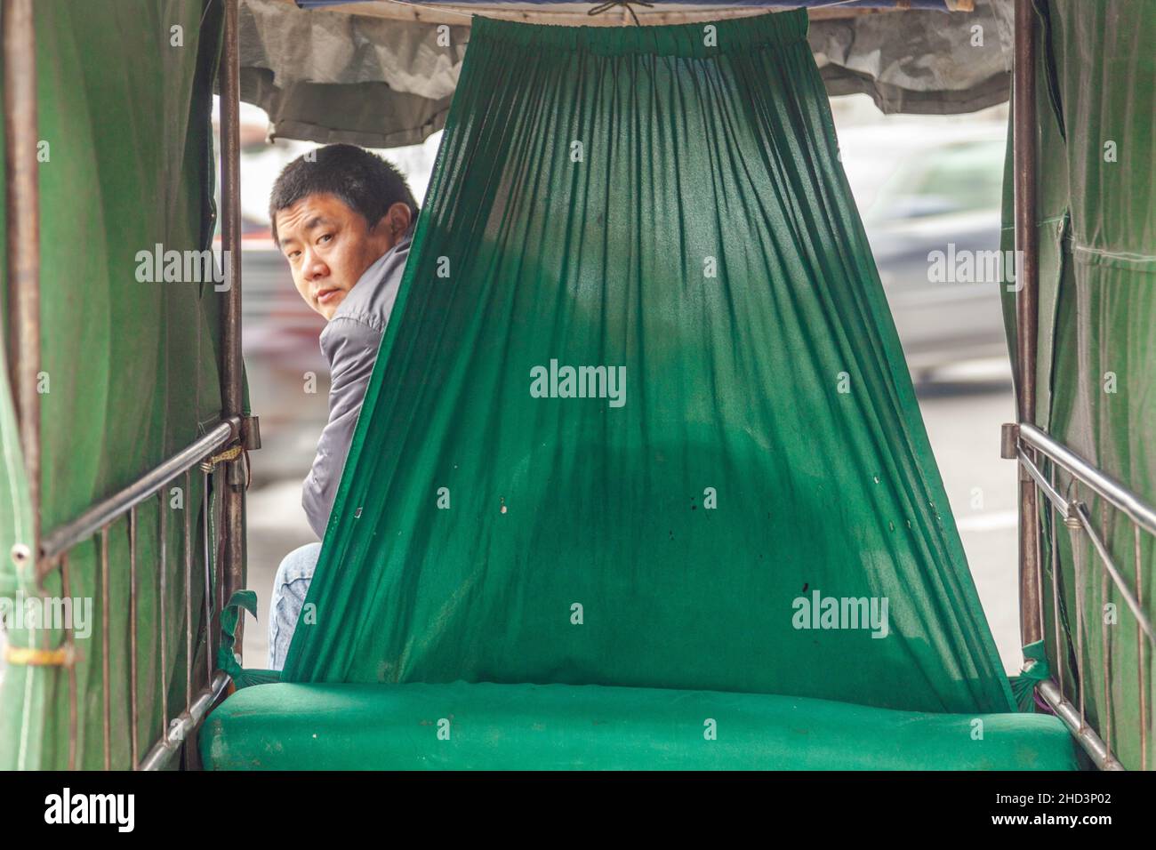 Risciò conducente guardando indietro. Tela verde. Jiashan, Cina Foto Stock