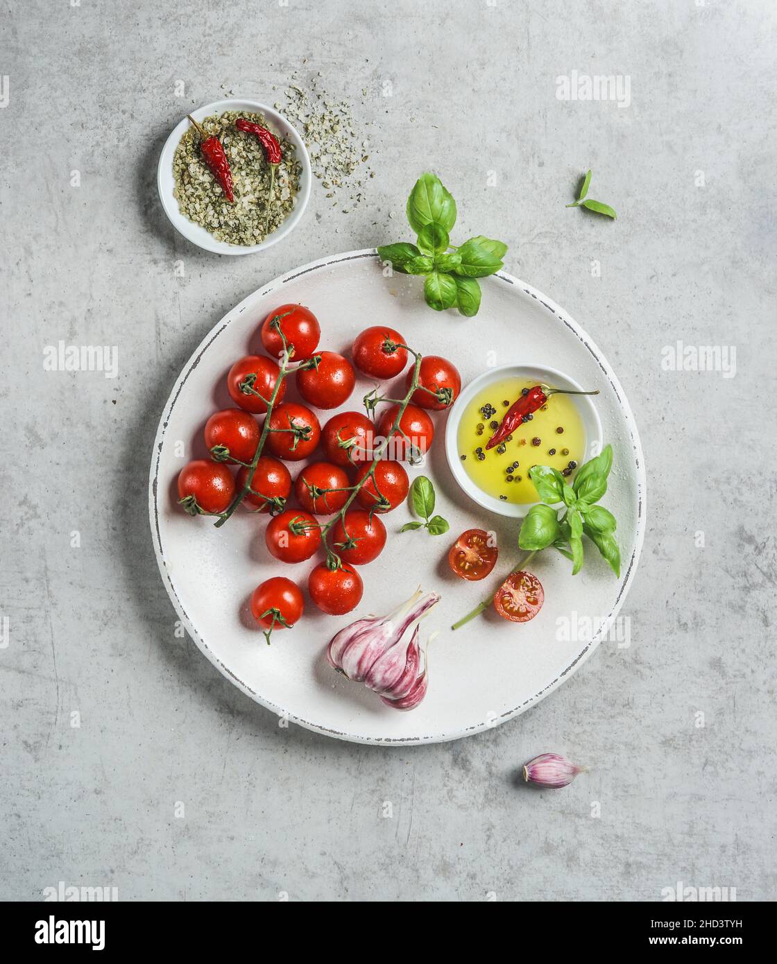 Ingredienti freschi e gustosi: Pomodori, ciotola con olio d'oliva, erbe, aglio e sale verde con peperoncino su piatto bianco. Vista dall'alto Foto Stock