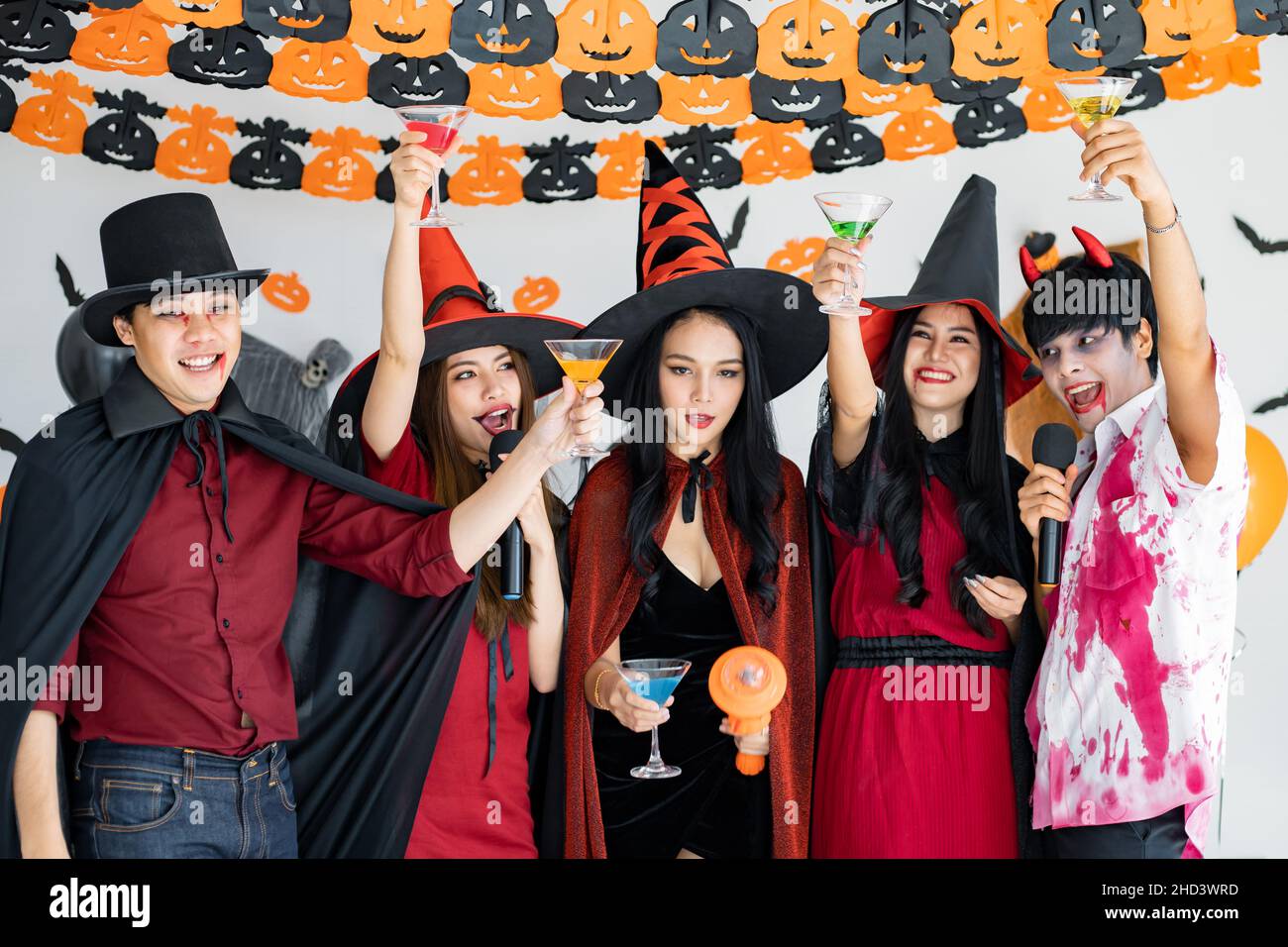 Banda di giovani asiatici in costume strega, strega con festa Halloween festa per cantare una canzone e una bevanda, dessert in camera. Gruppo teen thailandese con celebrità Foto Stock