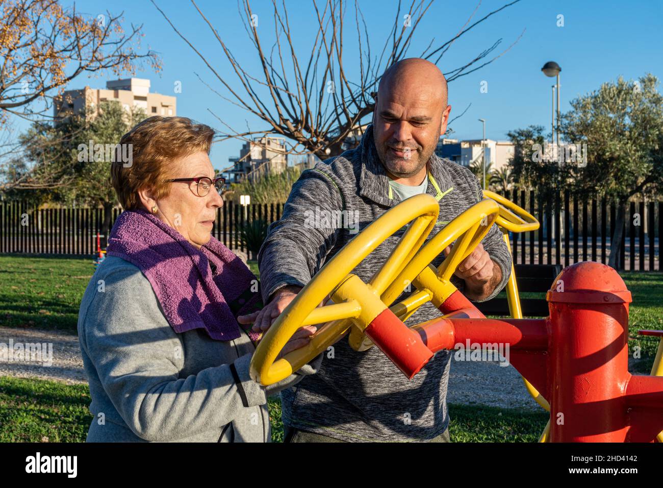 L'allenatore maschile aiuta la donna anziana ad esercitarsi sulla macchina in un parco bio-sano Foto Stock