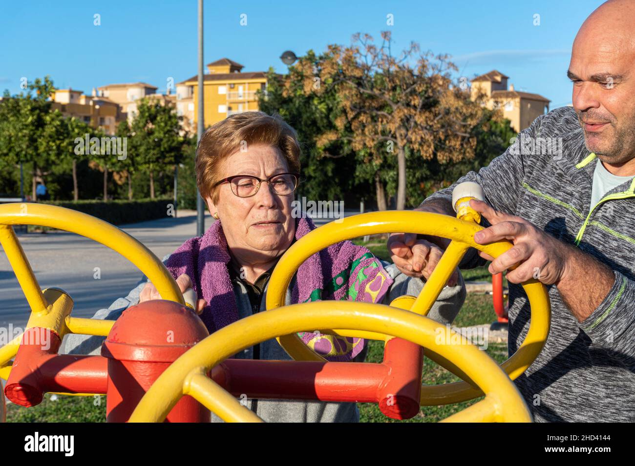 L'allenatore maschile aiuta la donna anziana ad esercitarsi sulla macchina in un parco bio-sano Foto Stock