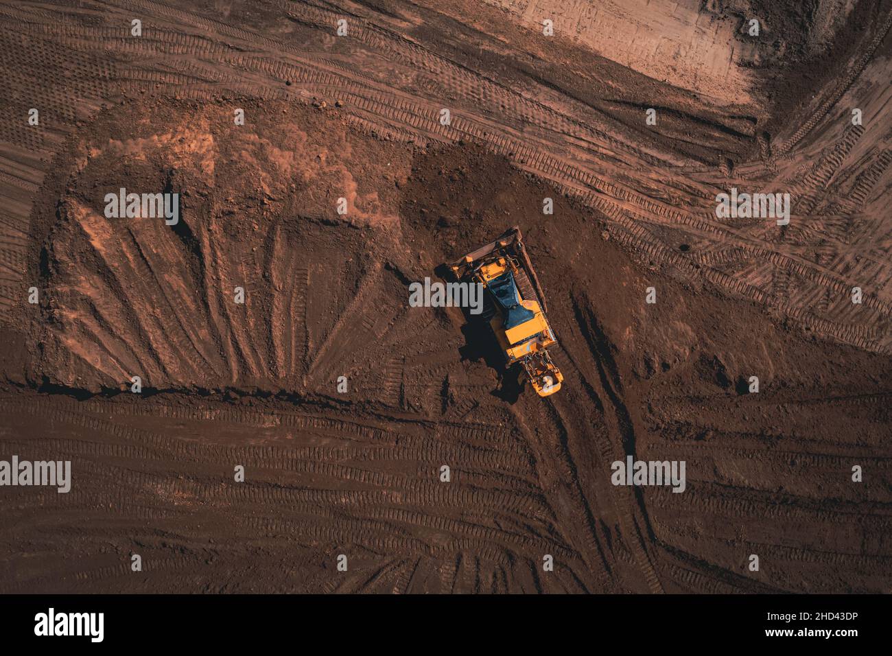 Il bulldozer cingolato giallo esegue lavori di terra - scatto con vista aerea. Il trattore cingolato giallo rastrema il terreno per costruire una strada asfaltata. Apripista terra lavora durante la costruzione della strada di percorso. Foto Stock
