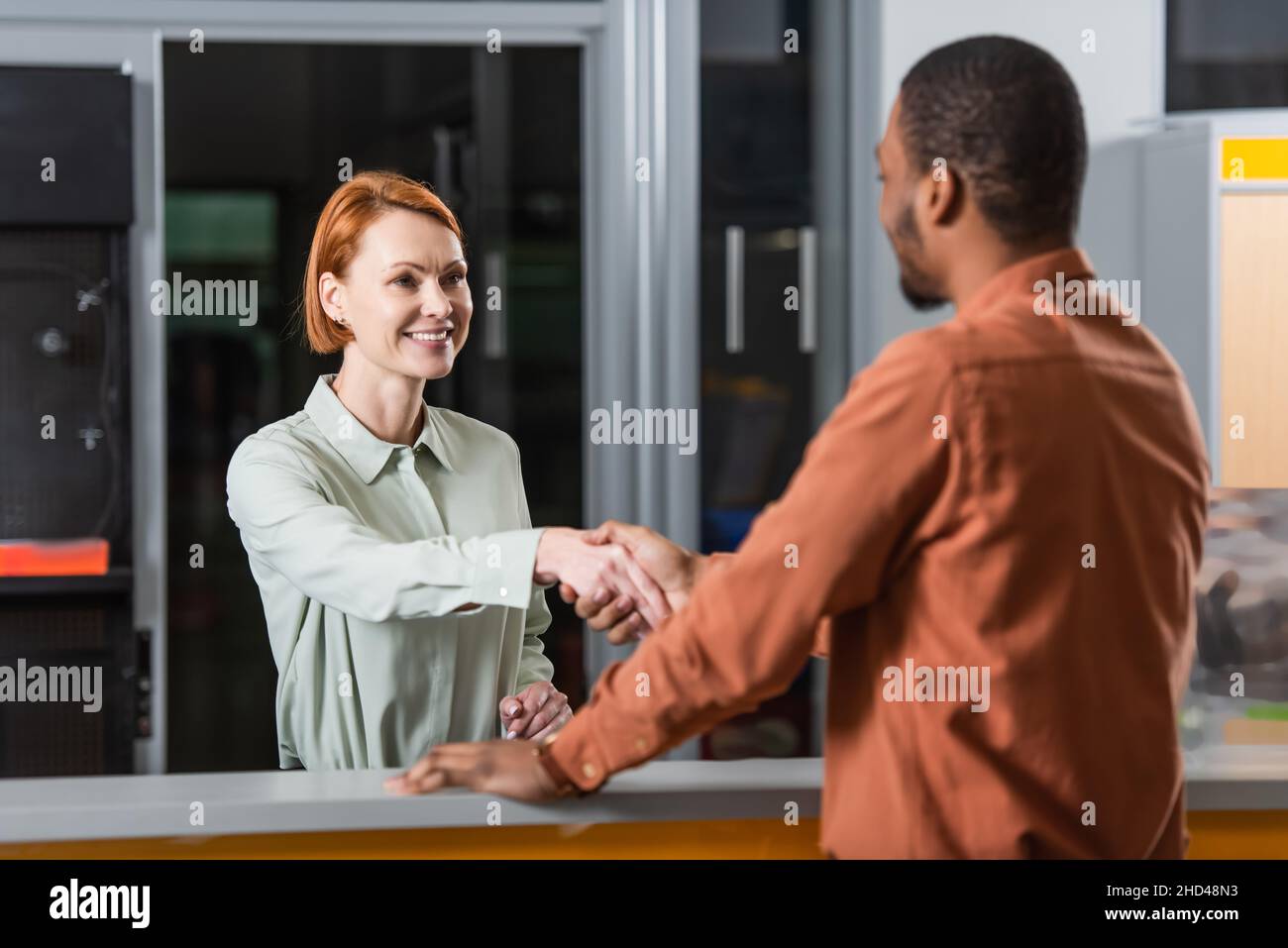 concessionario auto sorridente che scuote le mani con un cliente afro-americano sfocato Foto Stock