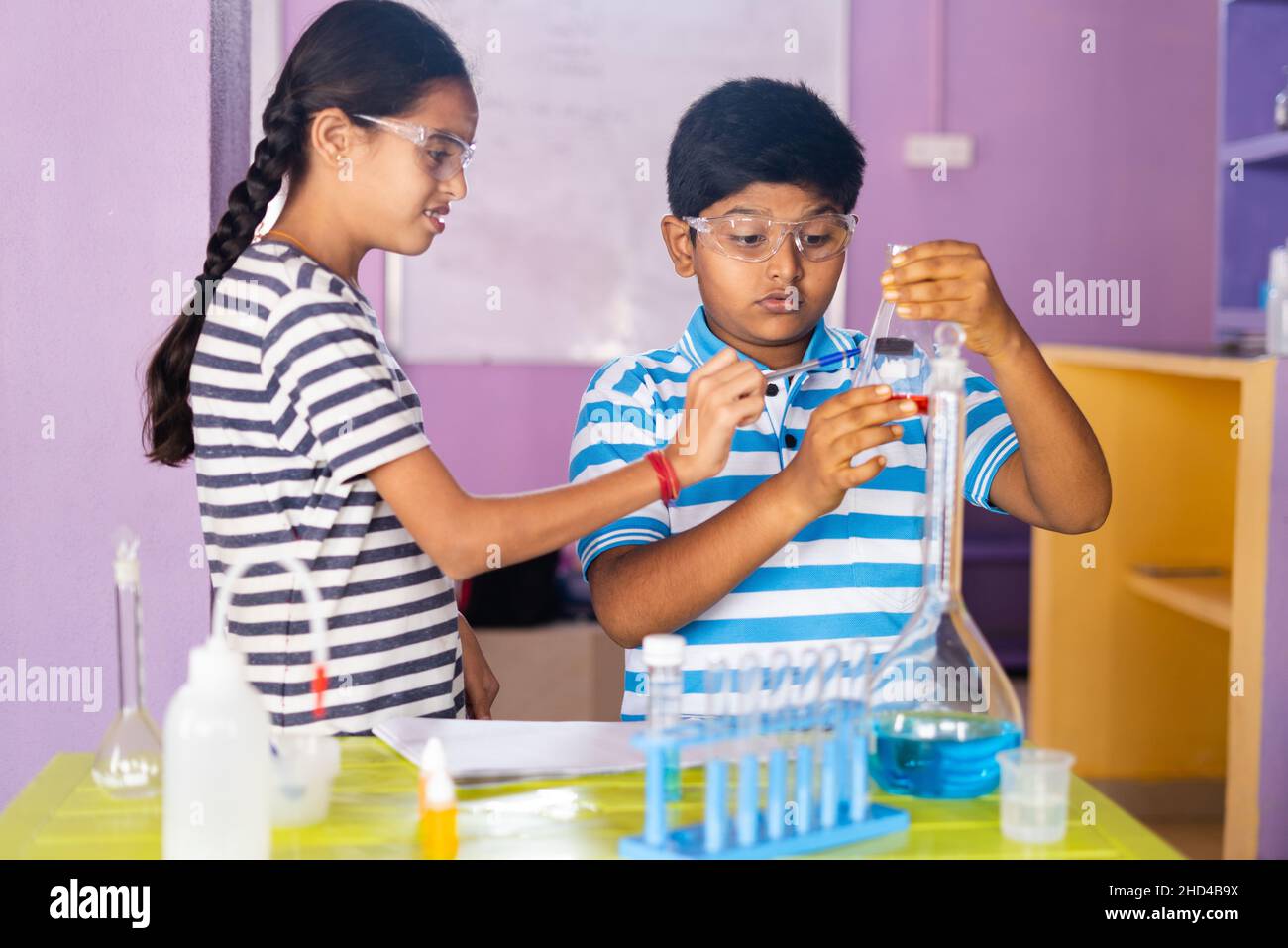 Primo piano di bambini concenterati che controllano o analizzano il chimical tenendo la fiasca mentre fanno l'esperimento al laboratorio di chimica Foto Stock