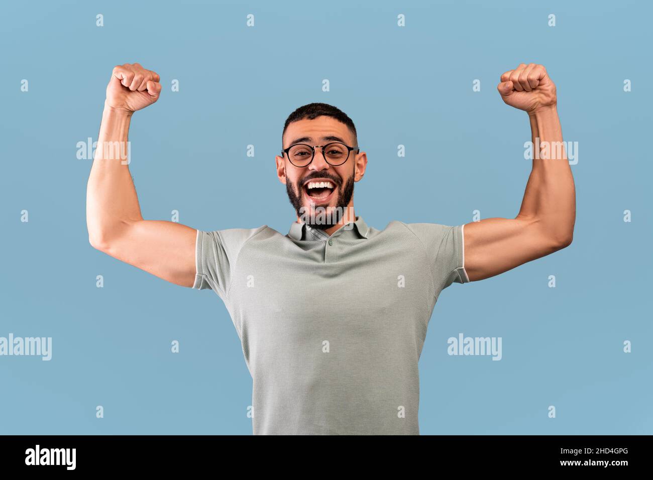 Concetto di vittoria e trionfo. L'uomo arabo pieno di gioia urlando di pugni aggrappati, alzati in aria, sfondo blu Foto Stock