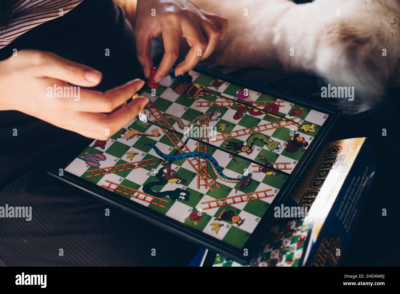 KORONADAL, PH – DEC 25, 2021:mano delle ragazze che gioca a Snakes and Ladgers gioco da tavolo AKA Moksha Patam, Chutes and Ladgers, o Bible UPS and Downs di 10x10 Foto Stock