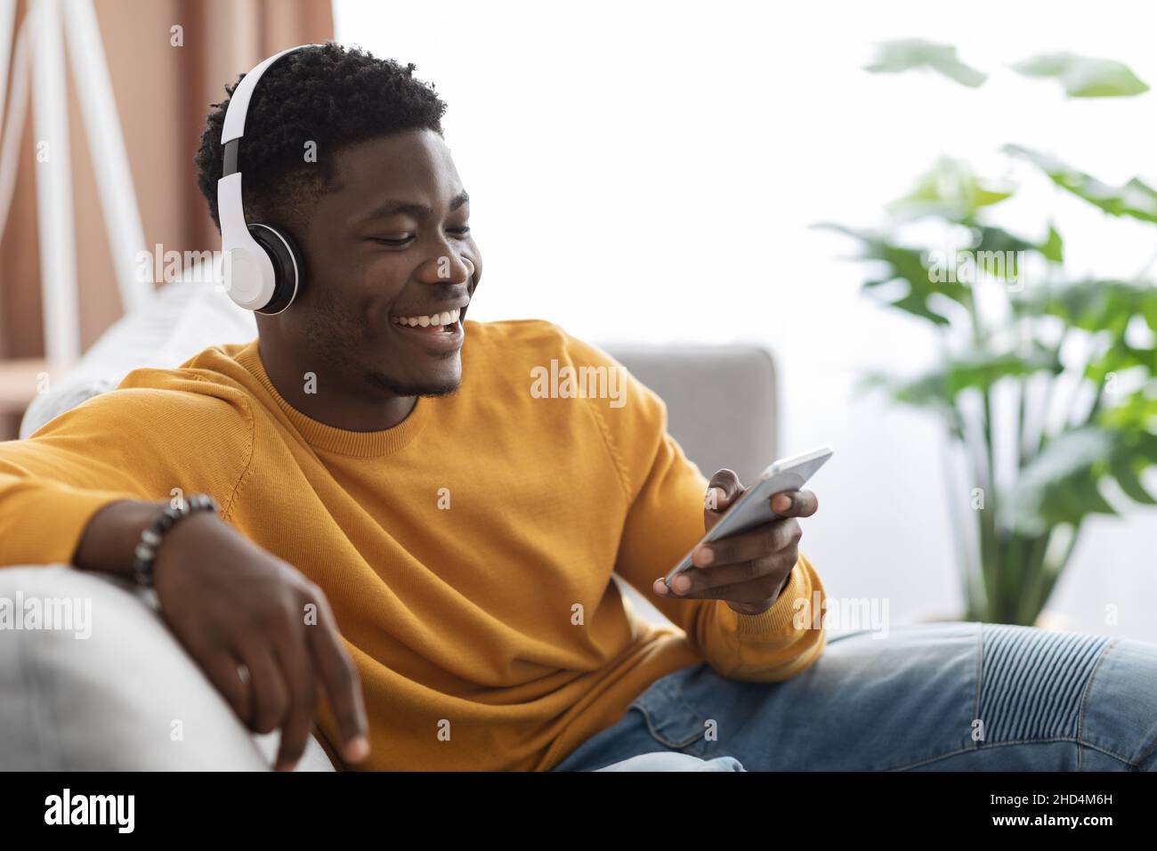 Felice ragazzo nero seduto sul divano, guardando video sullo smartphone Foto Stock