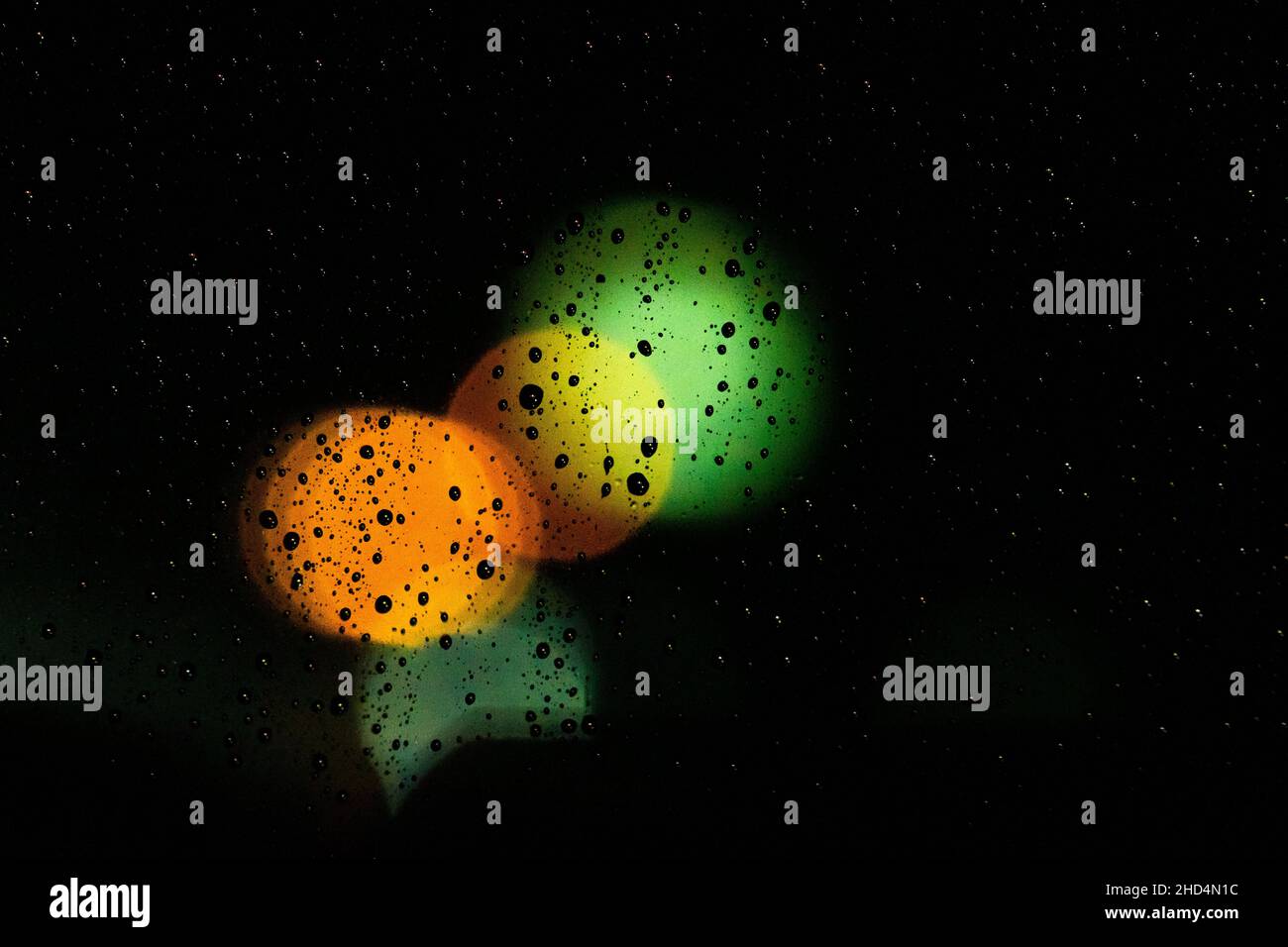 Primo piano di gocce di pioggia su un vetro che riflette le luci di notte Foto Stock