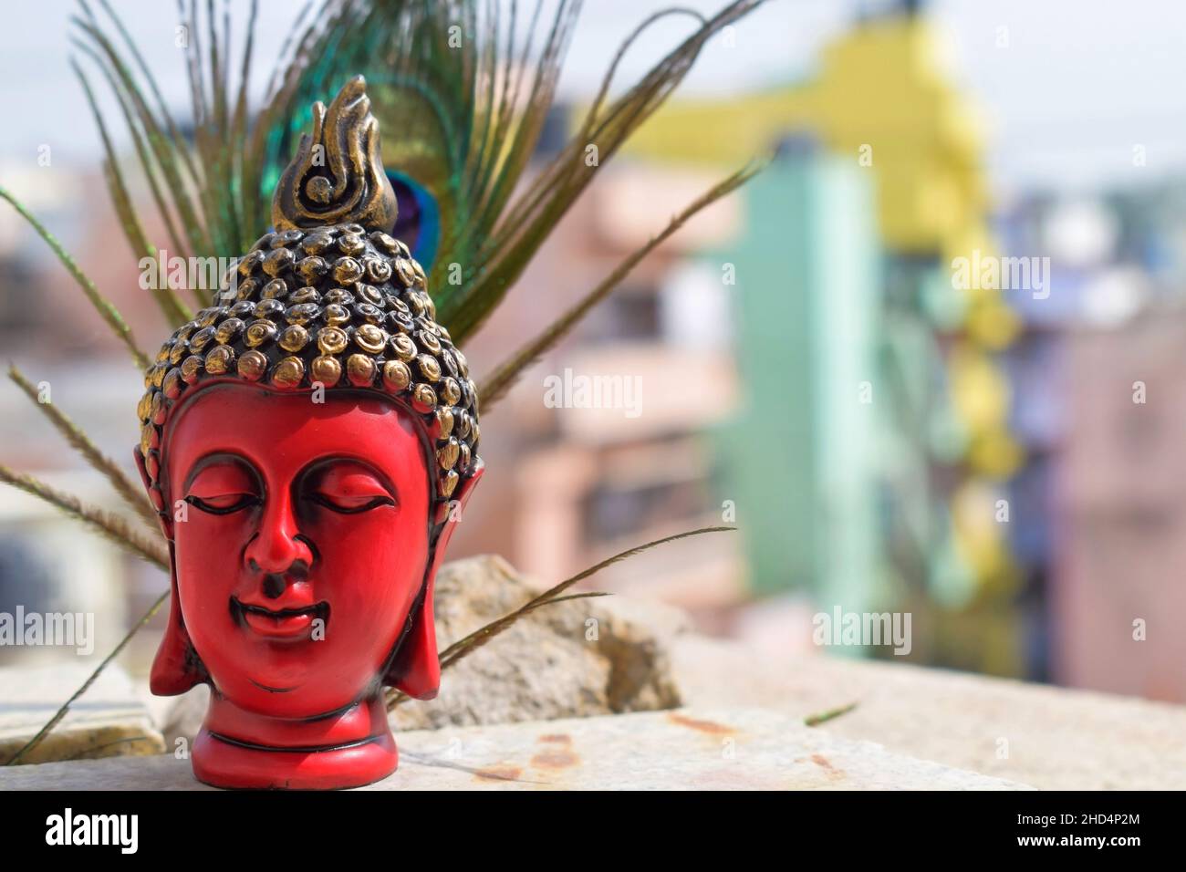 Bella scultura del viso di colore rosso o statua del signore buddha, testa di statua dipinta di colore nero e dorato su piuma di pavone con cielo sul backgro Foto Stock