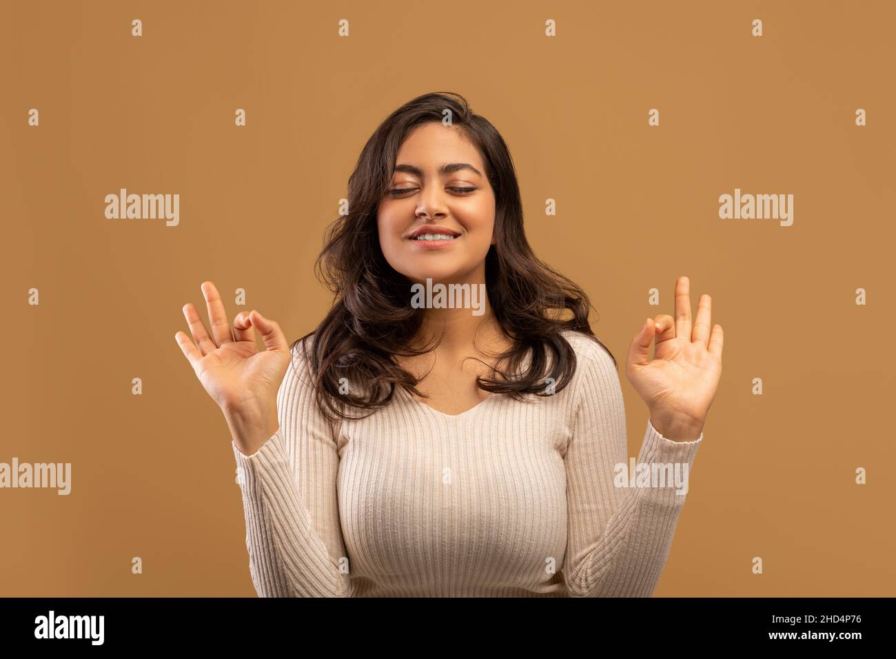 Concetto di meditazione. Donna araba pacifica facendo om gesto e meditando con gli occhi chiusi, sfondo beige Foto Stock
