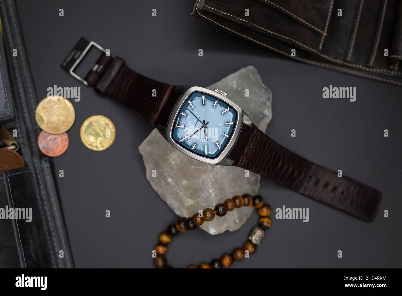 Vista dall'alto di un orologio Diesel con cintura in pelle su una pietra e braccialetto accanto alle monete su una superficie piana Foto Stock