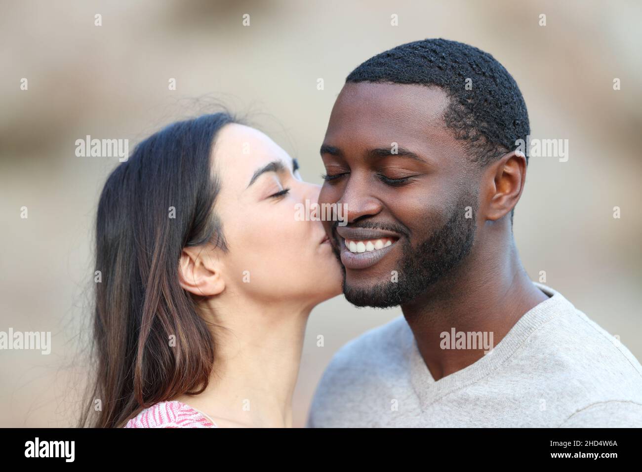 Felice donna caucasica baciare sulla guancia un uomo con la pelle nera Foto Stock