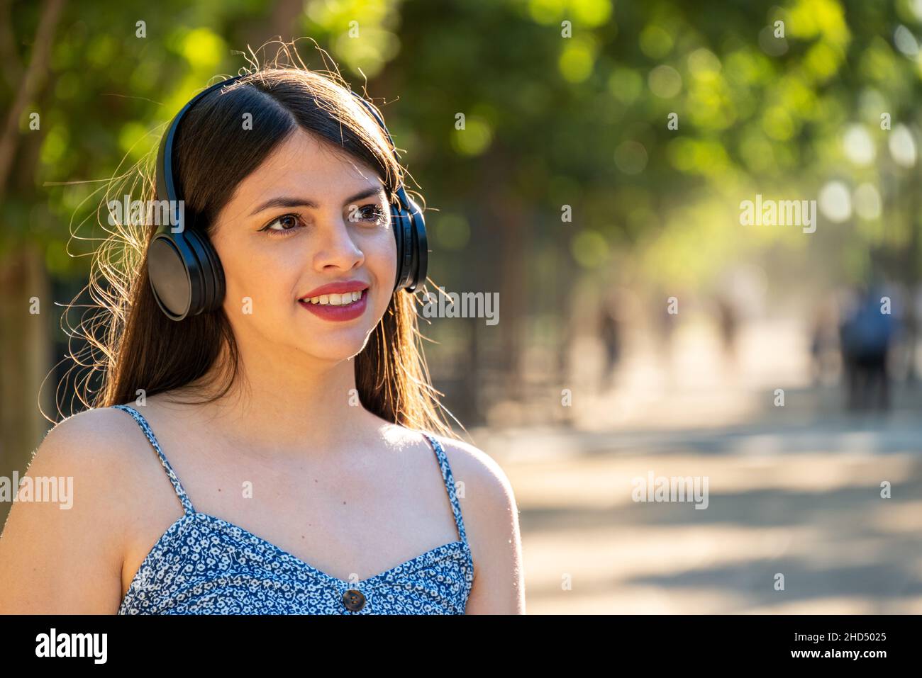 Giovane donna al parco con le cuffie per ascoltare la musica durante la giornata di sole durante la stagione primaverile estiva Foto Stock