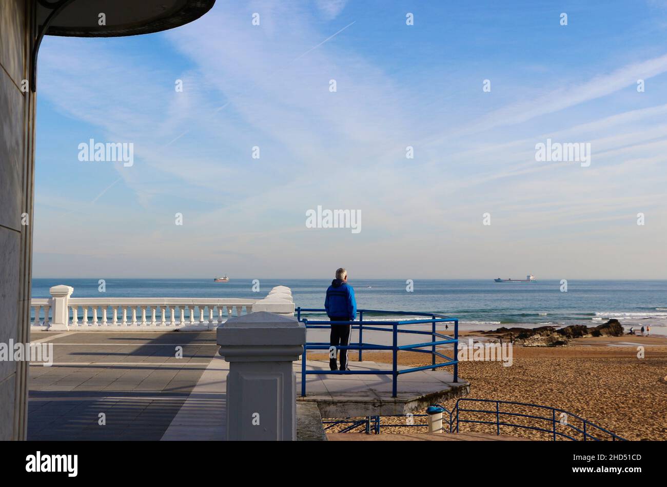 Uomo dai capelli grigi che indossa una tuta che guarda verso il mare a navi ancorate lontane al largo della costa di Santander Cantabria Spagna Inverno Foto Stock