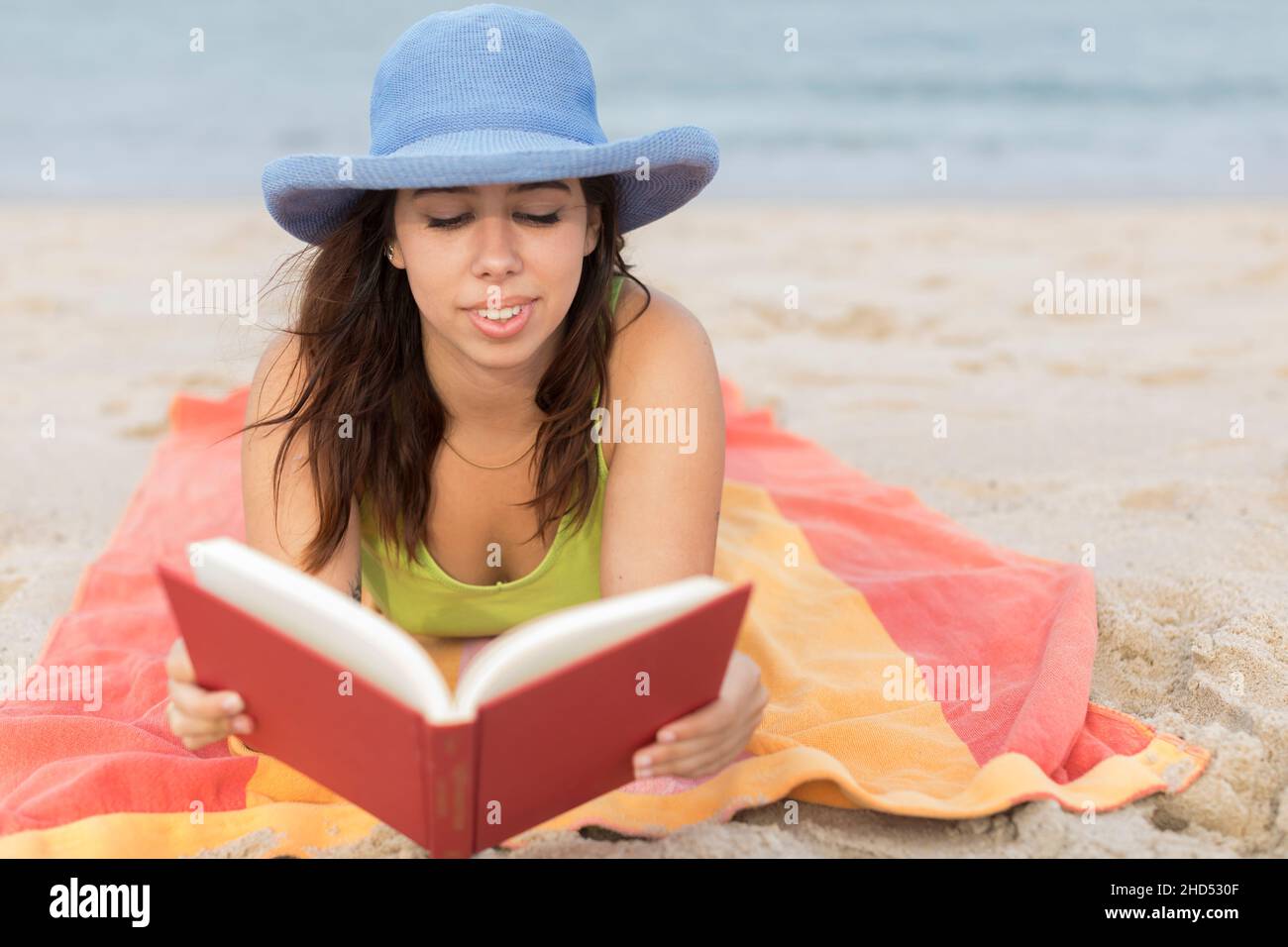 giovane donna in spiaggia su un asciugamano leggendo un libro Foto Stock