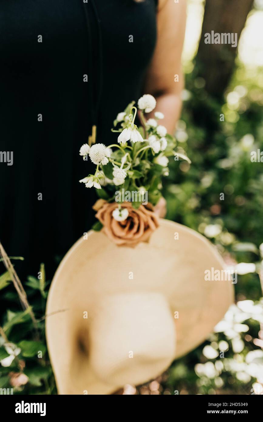 Primo piano di donna che tiene freschi fiori raccolti e grande cappello Foto Stock