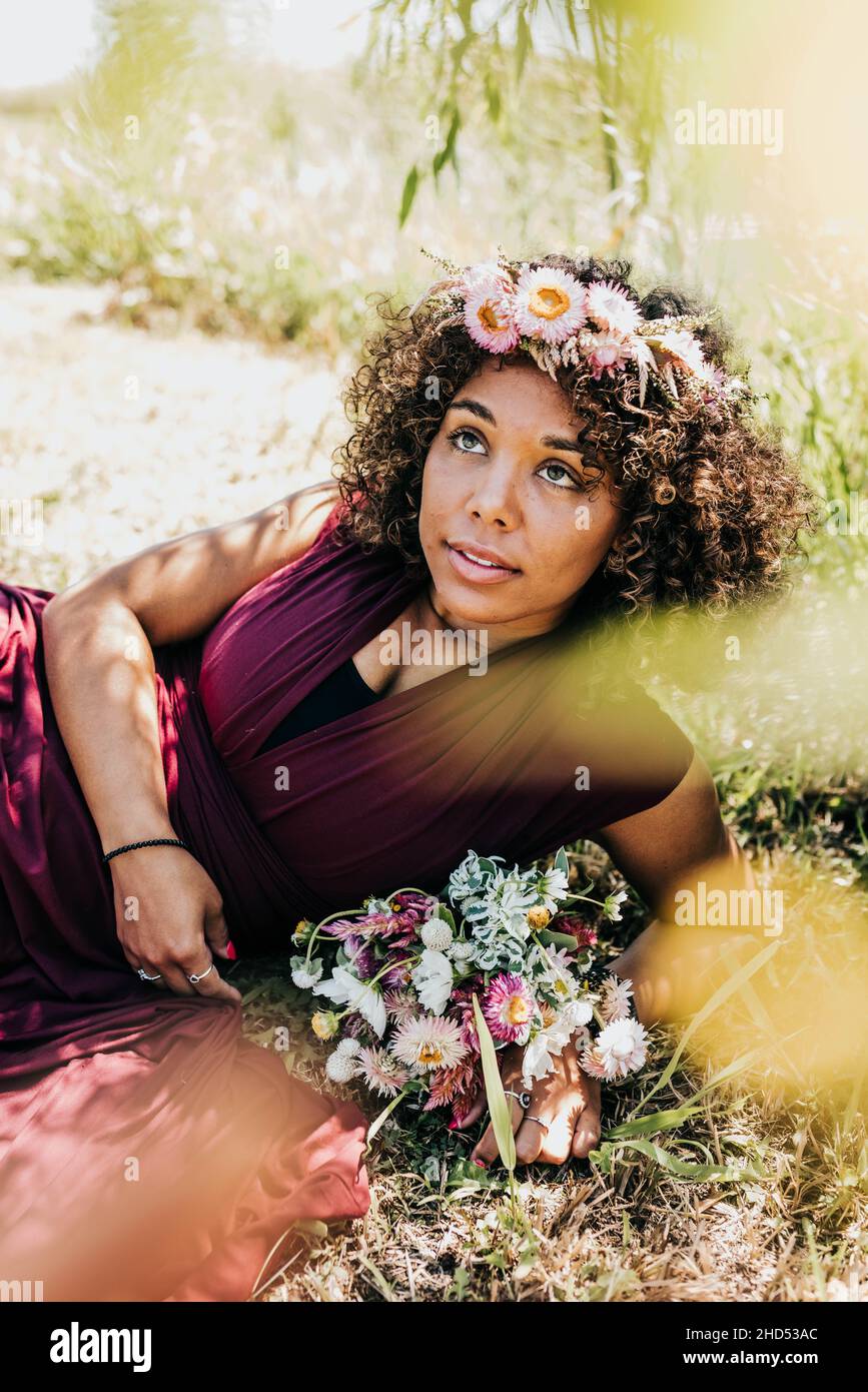 La donna si deposita in erba in abito da sposa e corona di fiori in estate Foto Stock