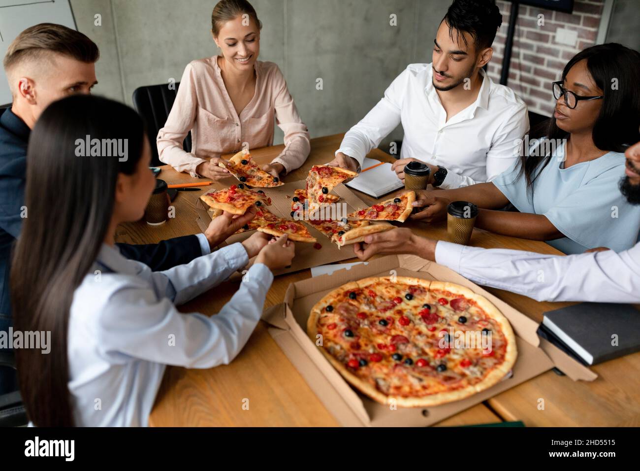 Gruppo di colleghi multietnici che si godono pranzo pausa in ufficio, mangiare pizza insieme Foto Stock