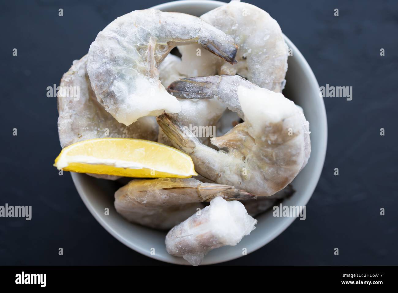 Gamberetti grandi congelati in ciotola grigia su sfondo nero con ghiaccio, limone per la cottura. Delizioso gamberetto senza testa per la preparazione del pasto. Goditi la natura Foto Stock