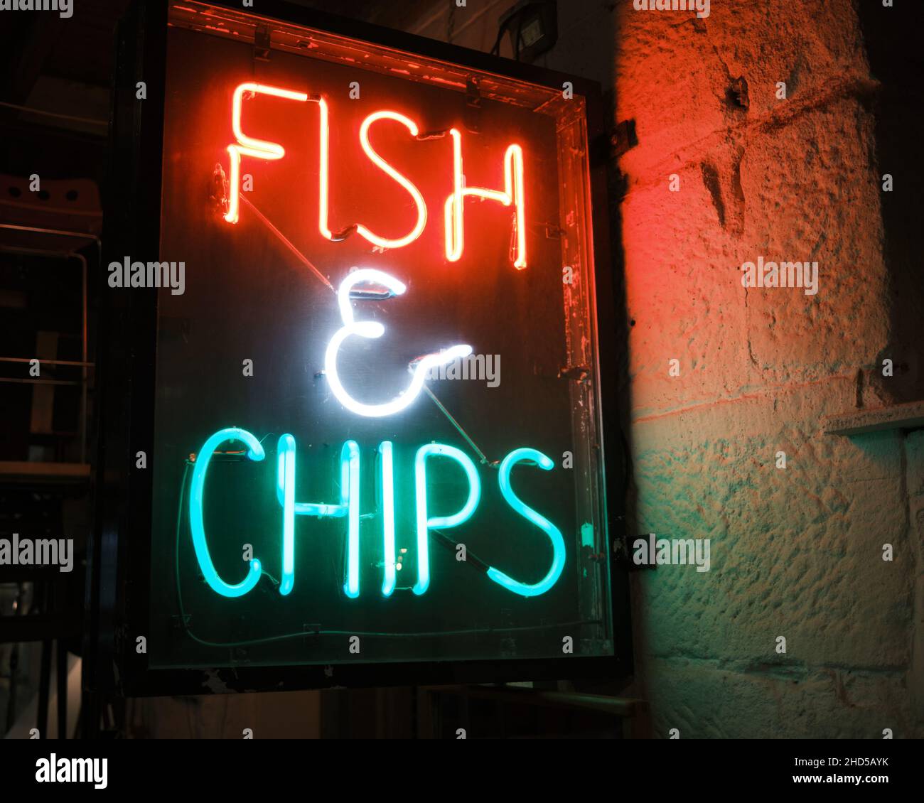 I pesci e le patatine al neon firmano in tubo al neon rosso e verde su una parete di pietra racchiusa in una scatola di vetro e legno Foto Stock