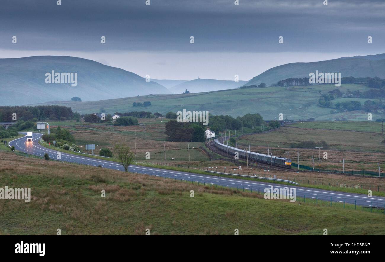 Il London - Glasgow & Edinburgh Caledonian Sleeper Train passa per Scout Green, Cumbria trainato da una locomotiva elettrica GBRF classe 92 accanto al M6 Foto Stock