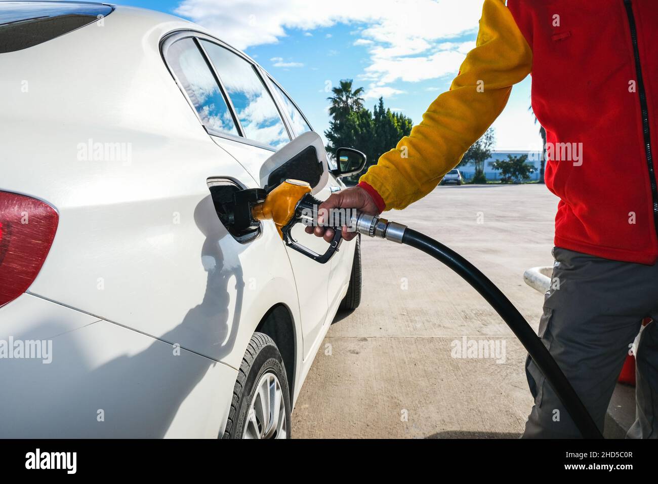 Uomo pompando benzina in auto alla stazione di benzina ed essendo riempire il serbatoio di gas di auto bianca in stazione di benzina, concetto di consumo di combustibile fossile globale. Foto Stock