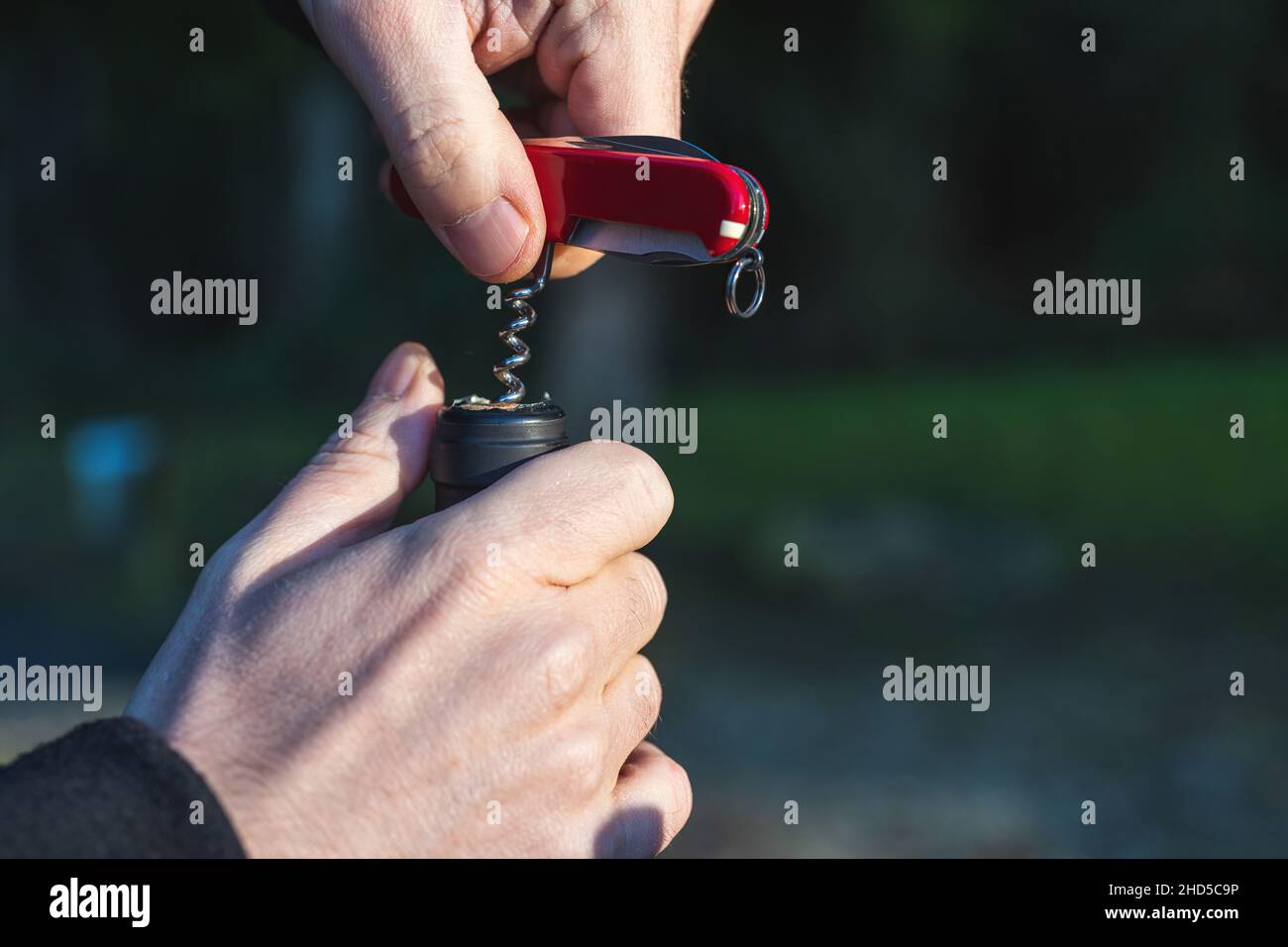 Apertura di una bottiglia di vino con un cavatappi a coltello tascabile. Primo piano al tramonto Foto Stock