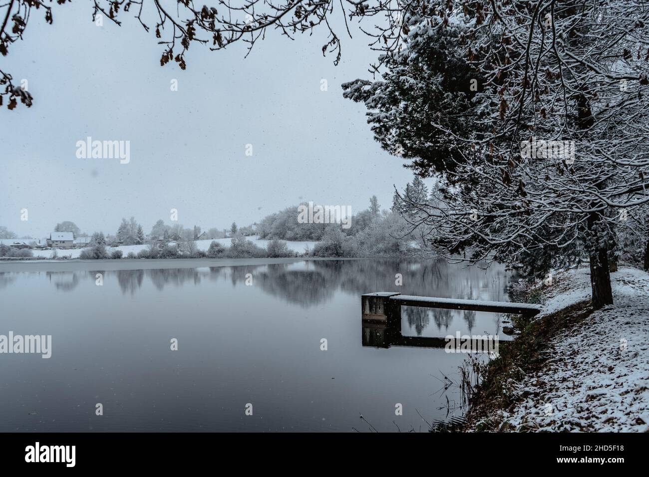 Molo di legno sul lago con neve fresca. Laghetto invernale con piccolo molo al mattino nebbioso. Paesaggio nuvoloso riflesso in acqua. Bianca campagna invernale Foto Stock