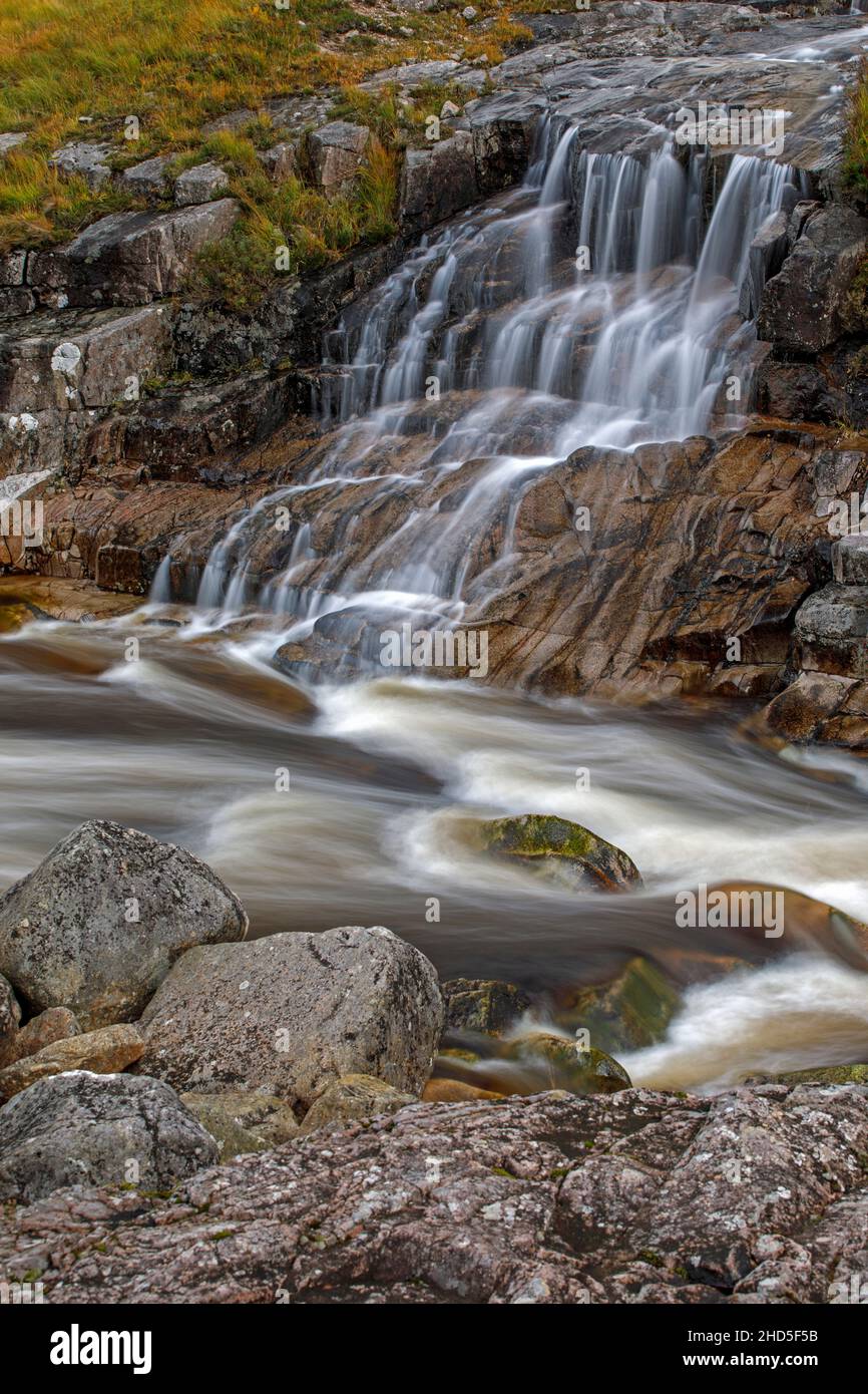 Un flusso affluente che cade in un fiume che scorre veloce. Foto Stock