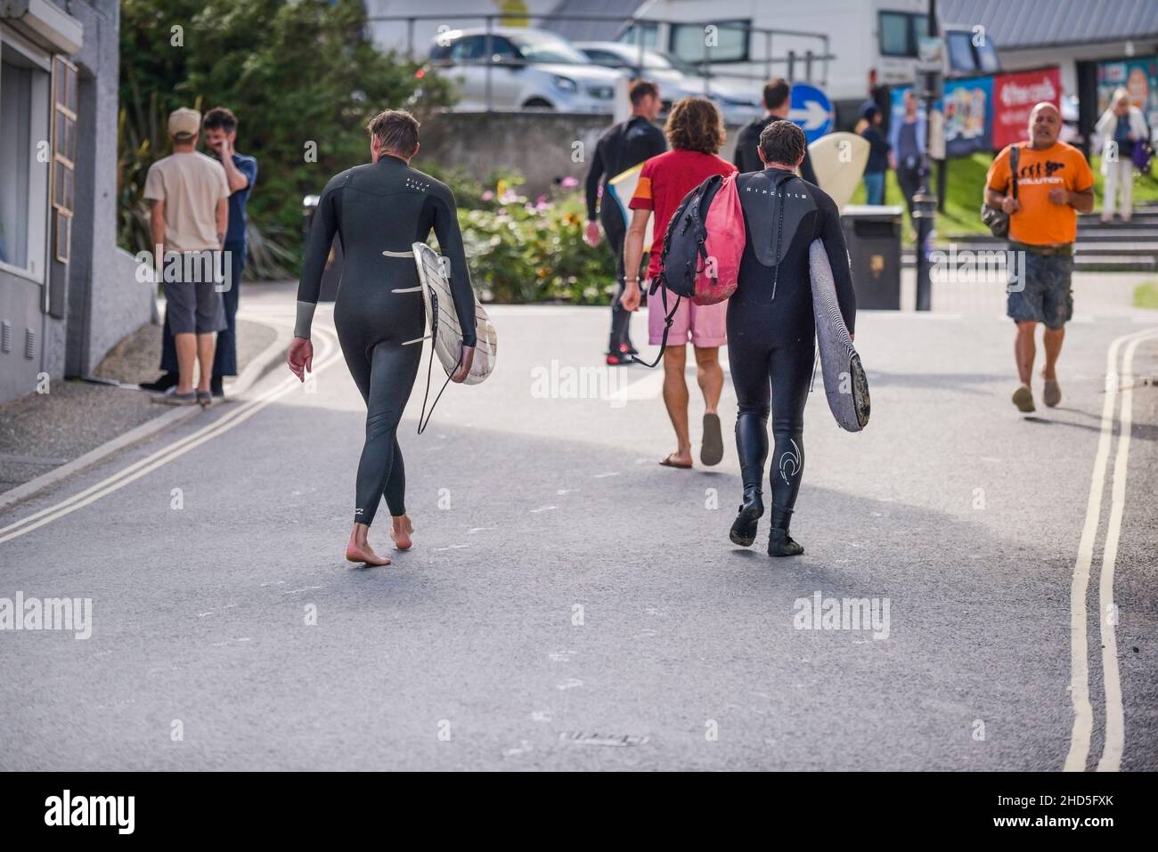 I surfisti portano le loro tavole da surf e camminano lungo una strada nel centro di Newquay Town in Cornovaglia. Foto Stock