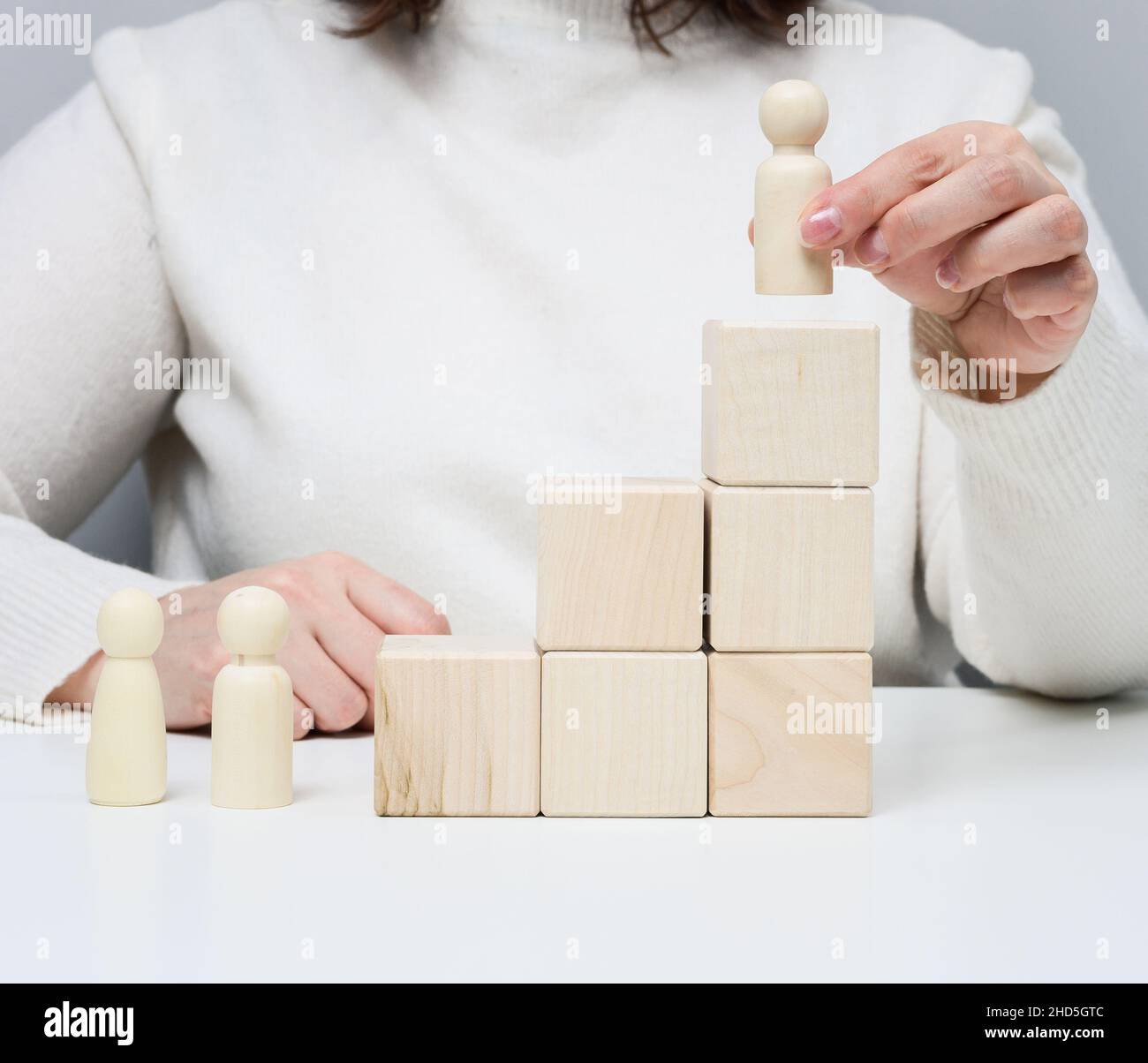 donna in un maglione bianco mette una figurina di legno sul podio. Il concetto di ricerca dei dipendenti, avanzamento di carriera. Dipendente di talento Foto Stock