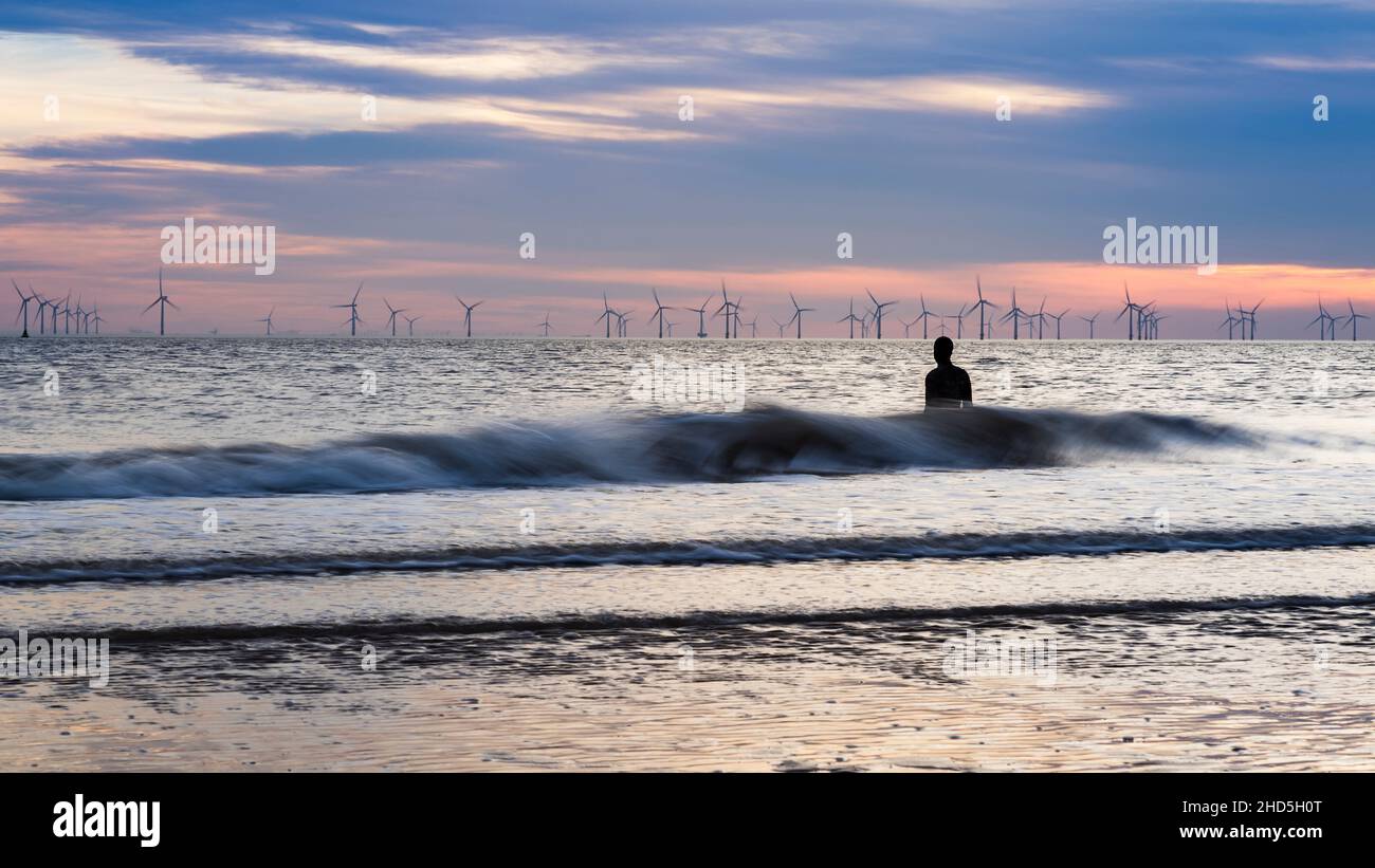 Le onde si tuffano contro un uomo di ferro in alta marea sulla spiaggia di Crosby in alta marea. Foto Stock