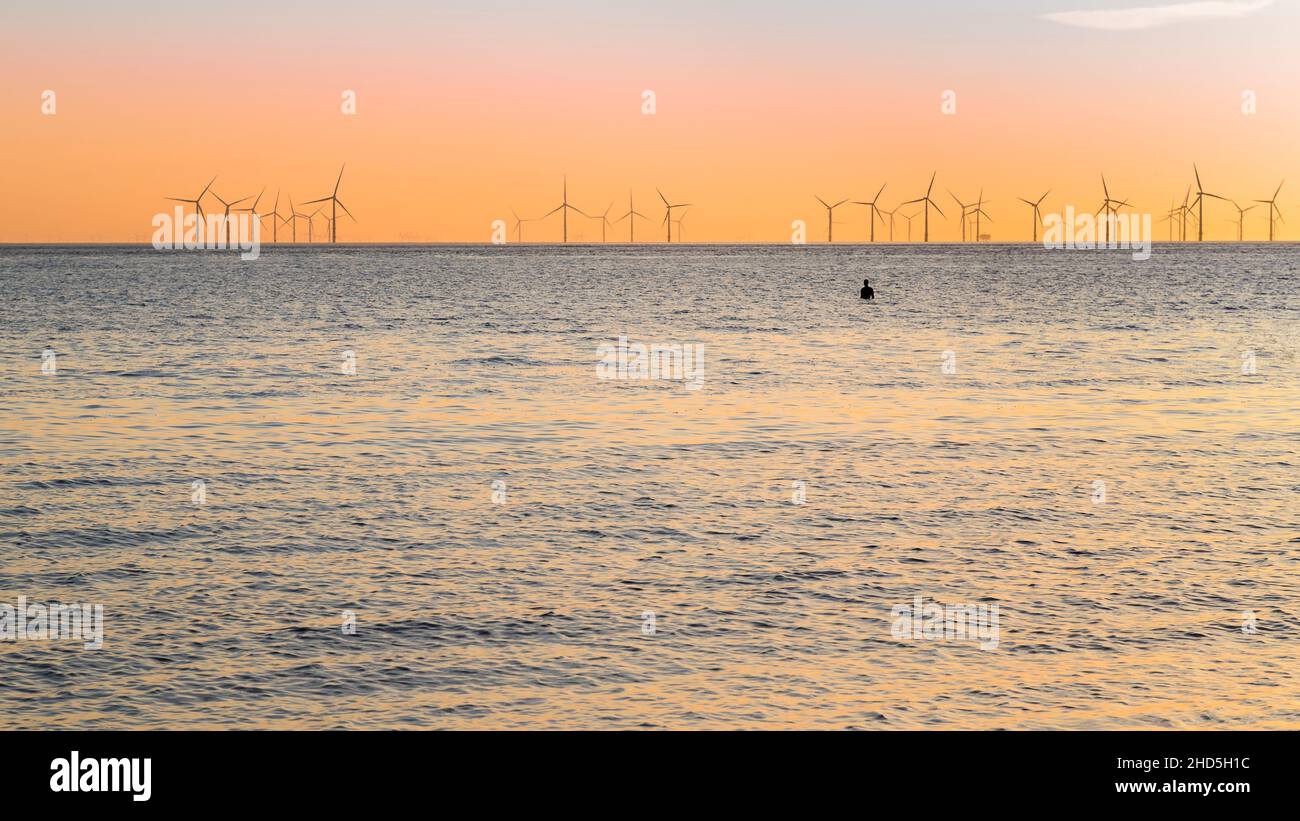 Un uomo di ferro isolato visto in alta marea sulla spiaggia di Crosby guardando il tramonto. Foto Stock