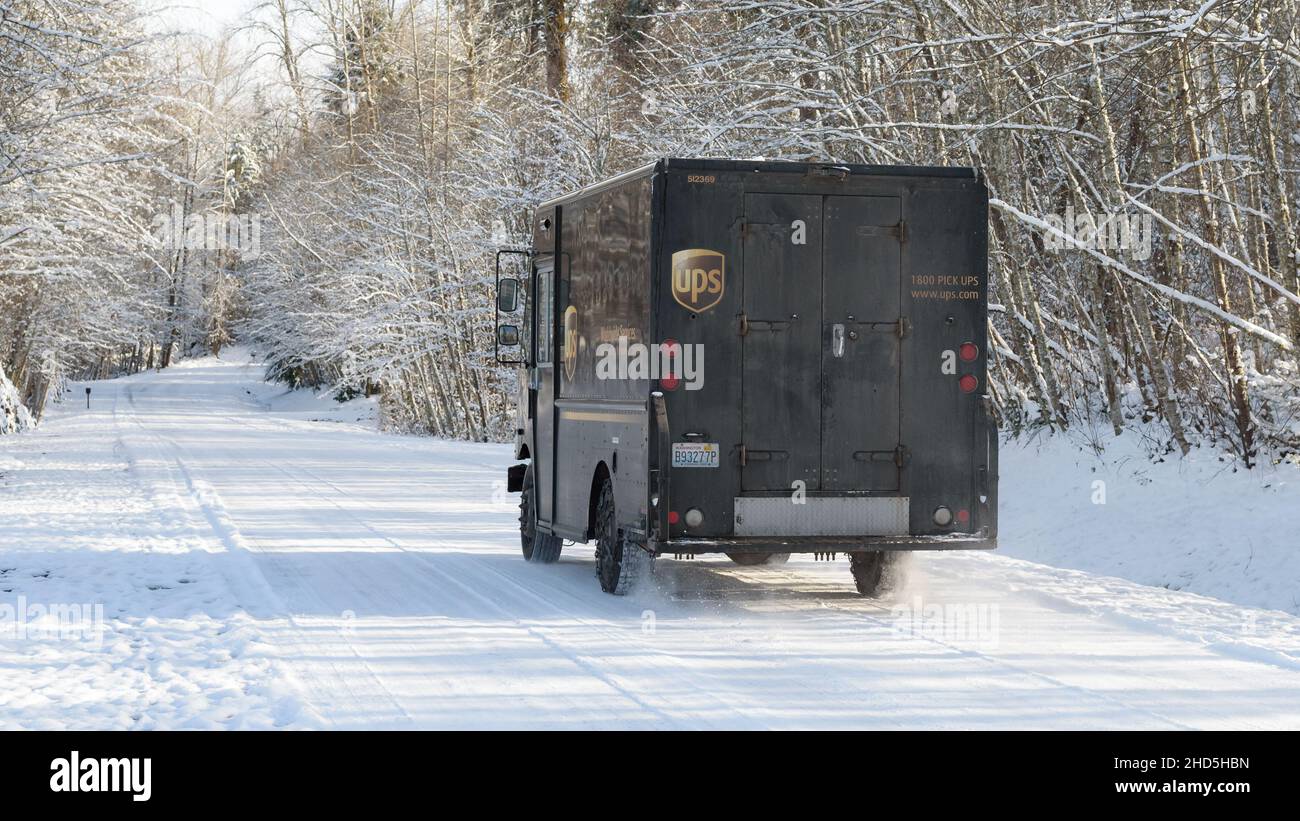Garofano, WA, USA - 29 dicembre 2021; Un camion di consegna UPS guida su una strada innevata con alberi invernali Foto Stock