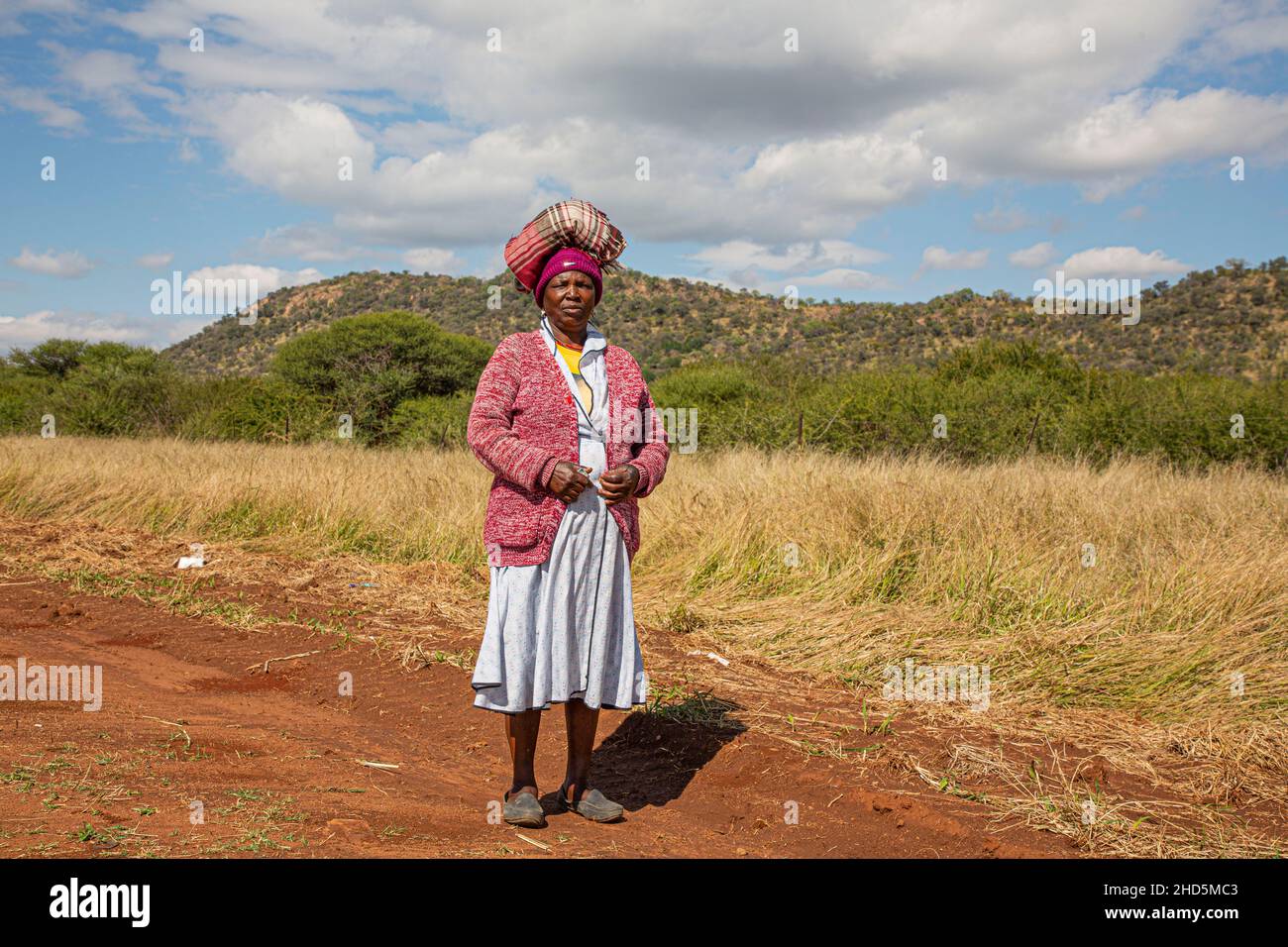 Signora africana che cammina lungo la strada equilibrando una coperta sulla sua testa Foto Stock