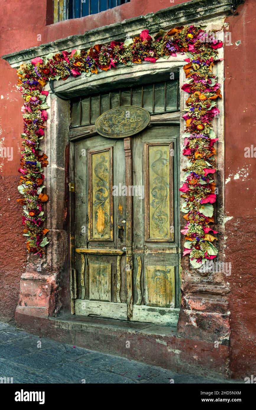 Una splendida entrata decorativa realizzata con fiori secchi che circondano la porta-telaio e antiche porte in legno presso la boutique a San Miguel de Allende, MX Foto Stock