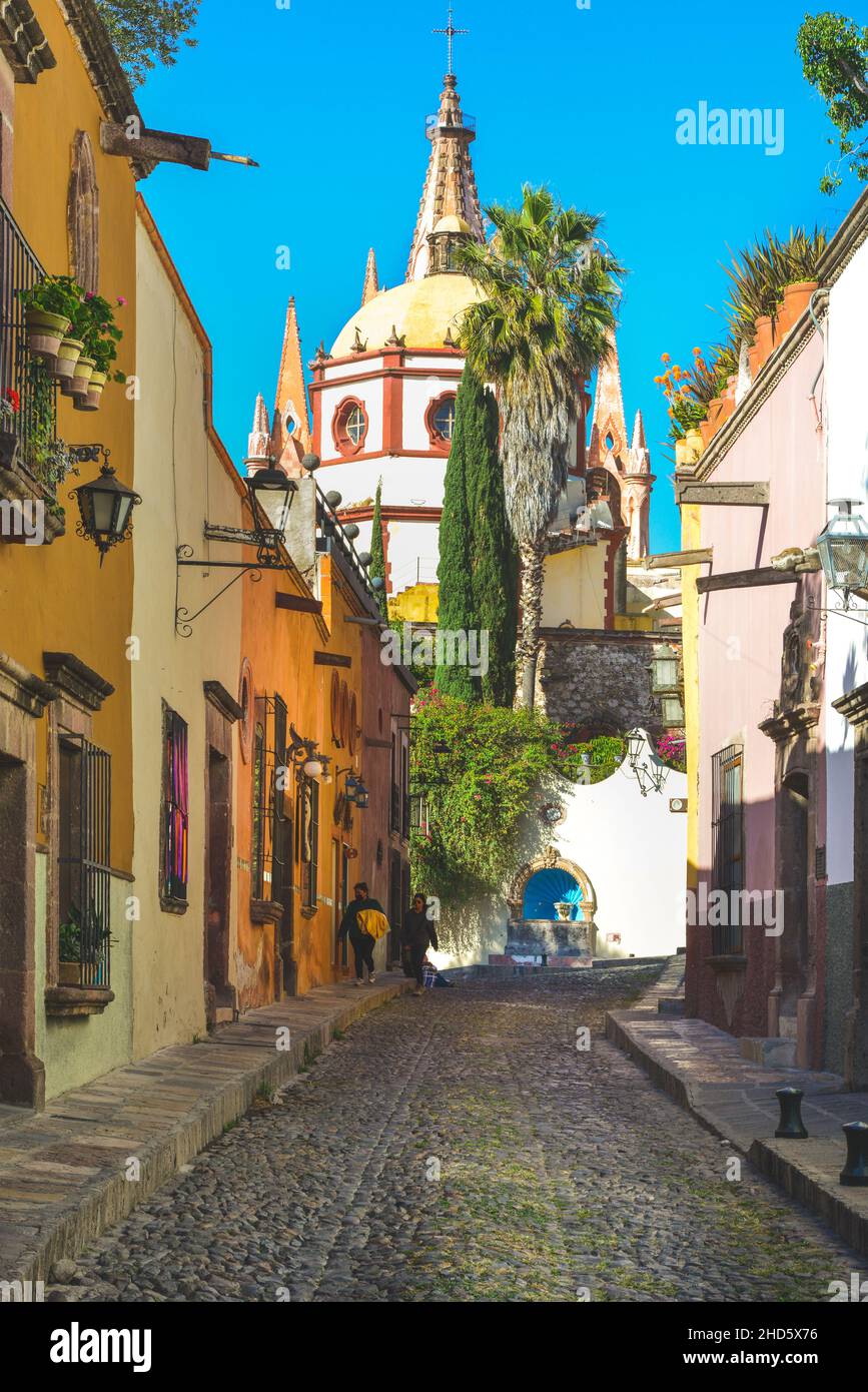 Stretta Cobblestone Aldama strada offre Vew della Parroquia San Miguel de Allende Arcangel Chiesa Dome accanto a case colorate in SMA, Messico Foto Stock