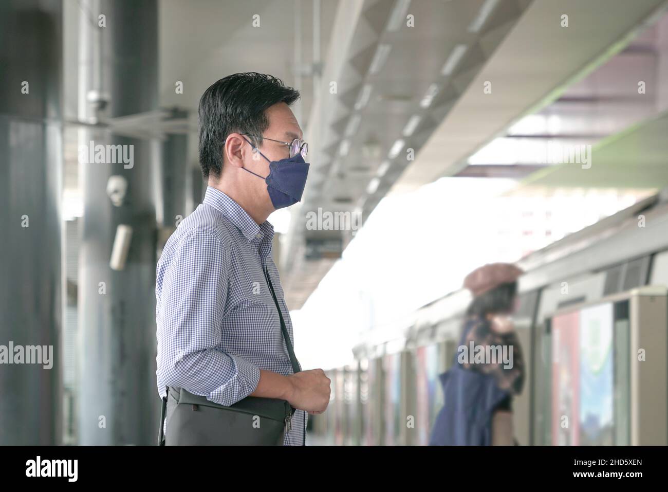 Uomo asiatico commuter con maschera facciale in piedi sulla piattaforma della metropolitana in attesa di entrare in treno. Concetto di transito mascherato. Foto Stock