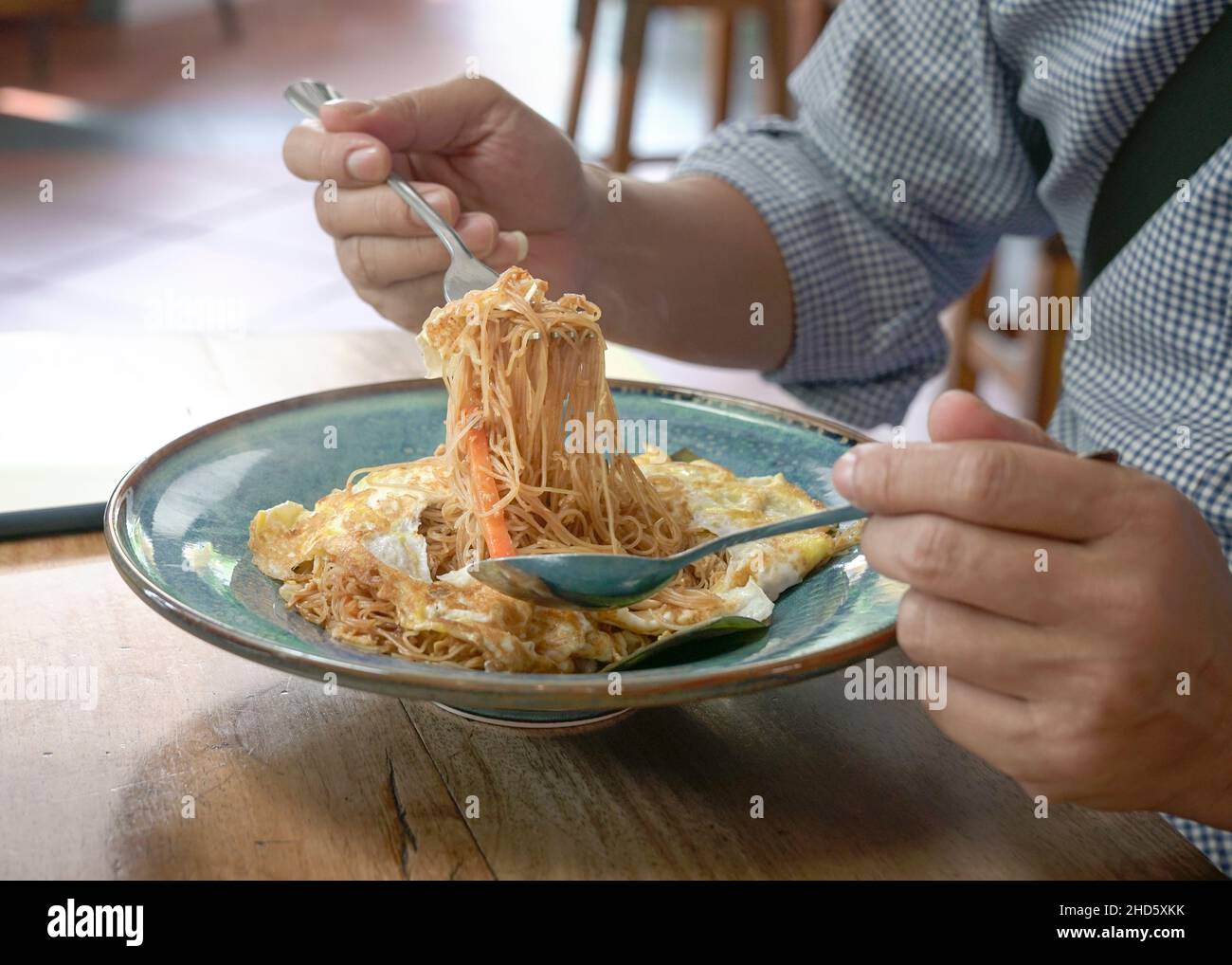 Uomo che mangia mescolare friggere tagliatelle avvolto con omellete uovo. Vista ravvicinata. Foto Stock