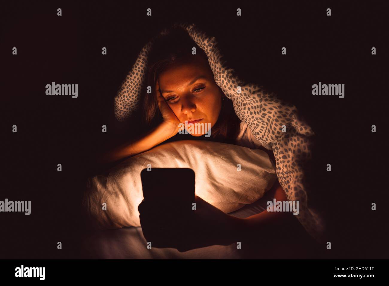 Giovane donna sdraiata a letto e con smartphone durante la notte prima di dormire. Dipendenza dai social media e insonnia Foto Stock