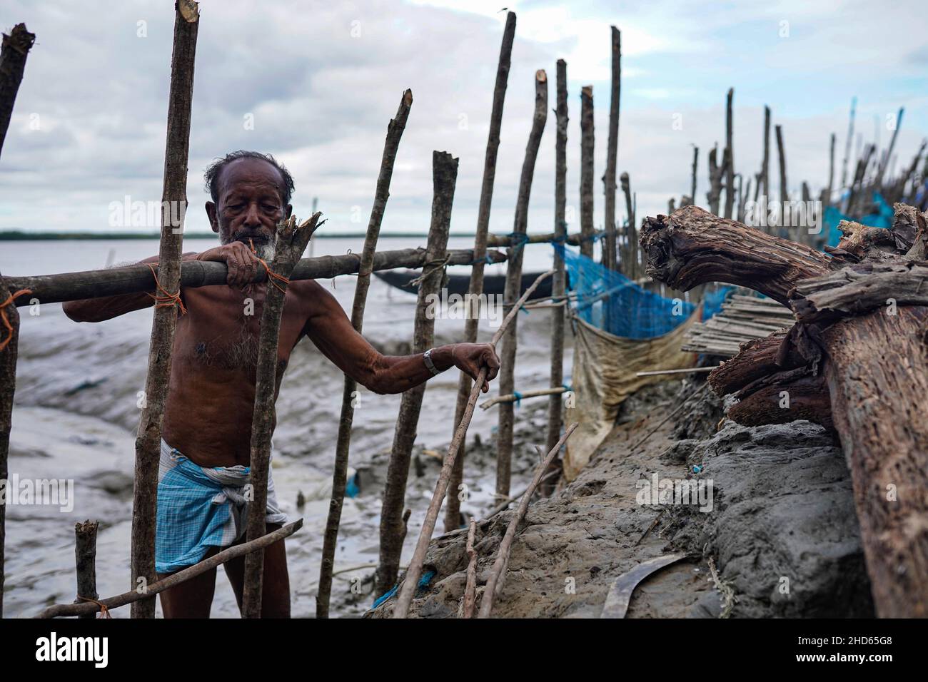 Un vecchio uomo ha visto ristabilire la recinzione per proteggere l'imbarco che è stato rotto da maree alte nella zona costiera del villaggio di Jaymani.Bangladesh è uno dei paesi più vulnerabili agli effetti del cambiamento climatico. I rischi naturali regolari e gravi che il Bangladesh già soffre di cicloni tropicali, maree elevate, erosione fluviale, alluvioni, frane e siccità sono tutti in grado di aumentare in intensità e frequenza a causa dei cambiamenti climatici. Foto Stock