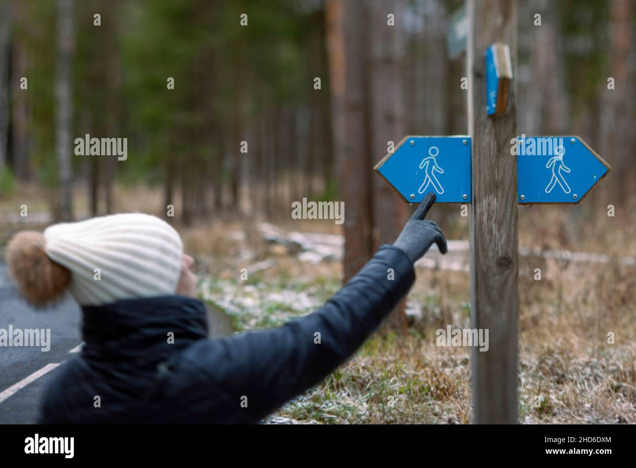 Una donna in abiti caldi vicino a un cartello che sceglie la direzione per escursioni, scena invernale, poco profondo DOF Foto Stock