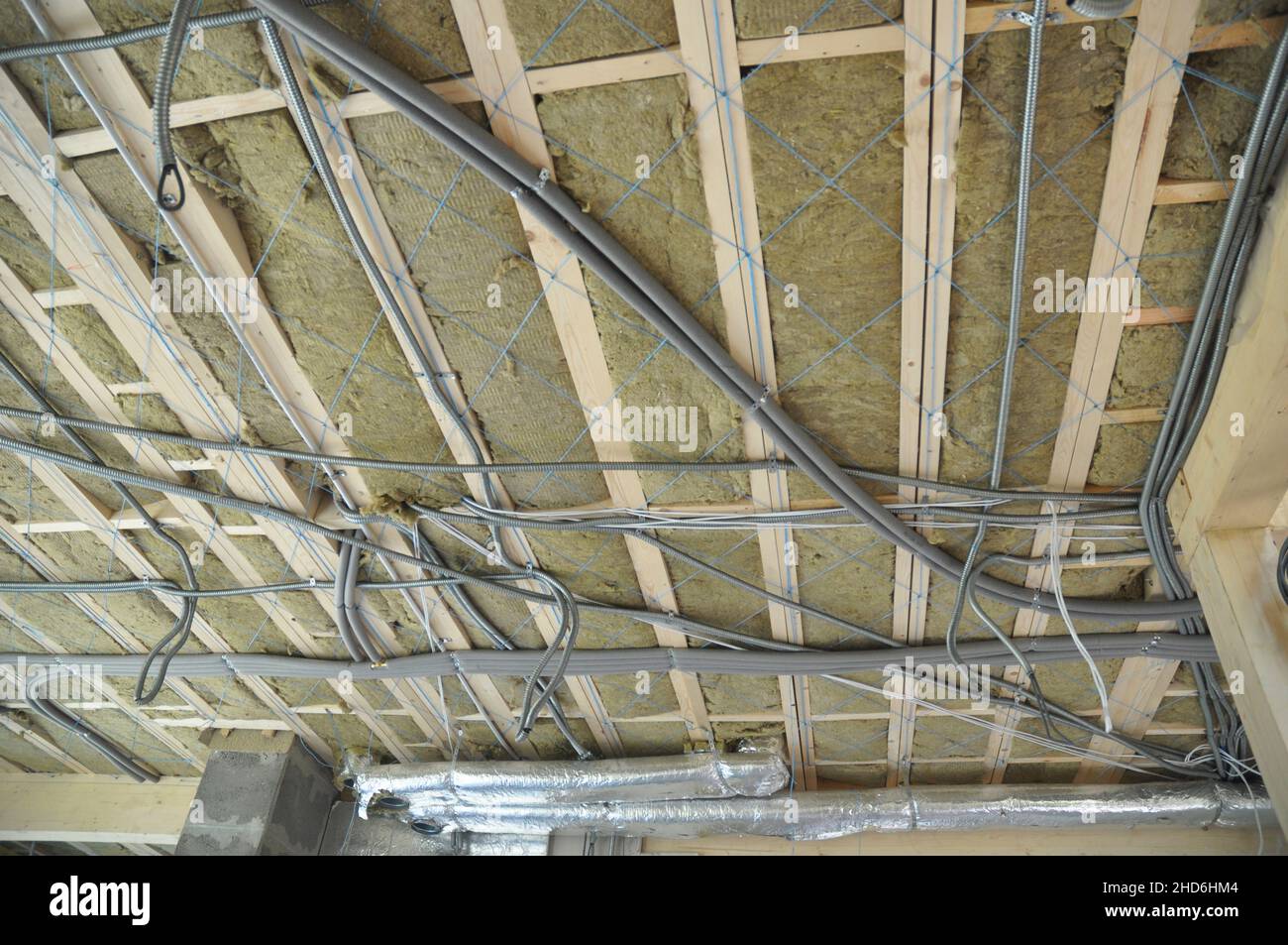 Isolamento in lana minerale da soffitto con tubi di ventilazione e cablaggio elettrico, cavi di alimentazione in tubo in pvc installati sul soffitto durante la casa Foto Stock