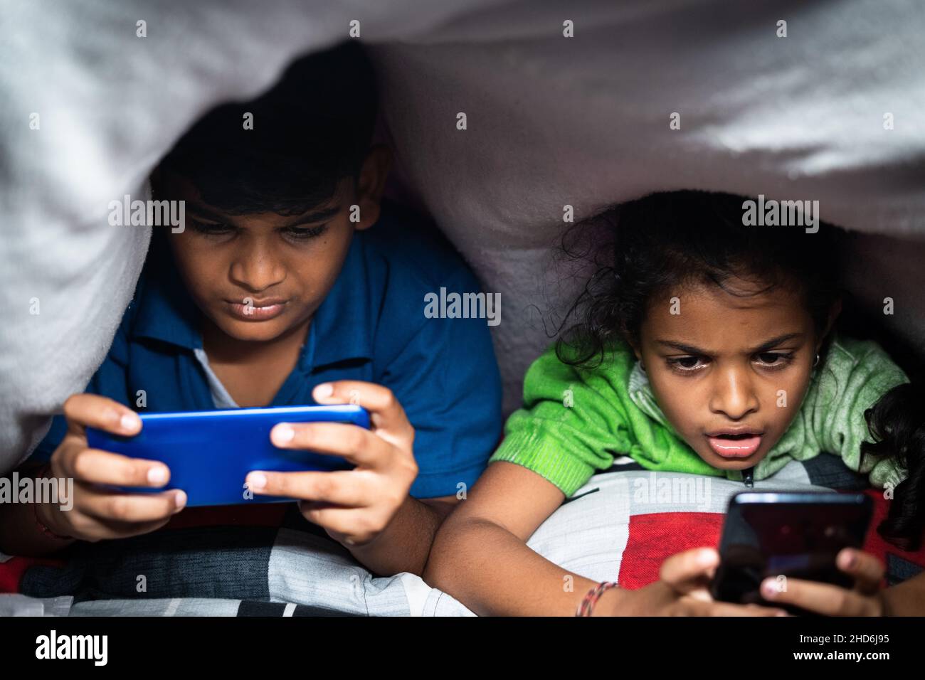 Bambini impegnati a giocare video gioco sul telefono cellulare di notte sotto il lenzuolo - concetto smartphone e tecnologia dipendenza, stile di vita infantile insalubre Foto Stock